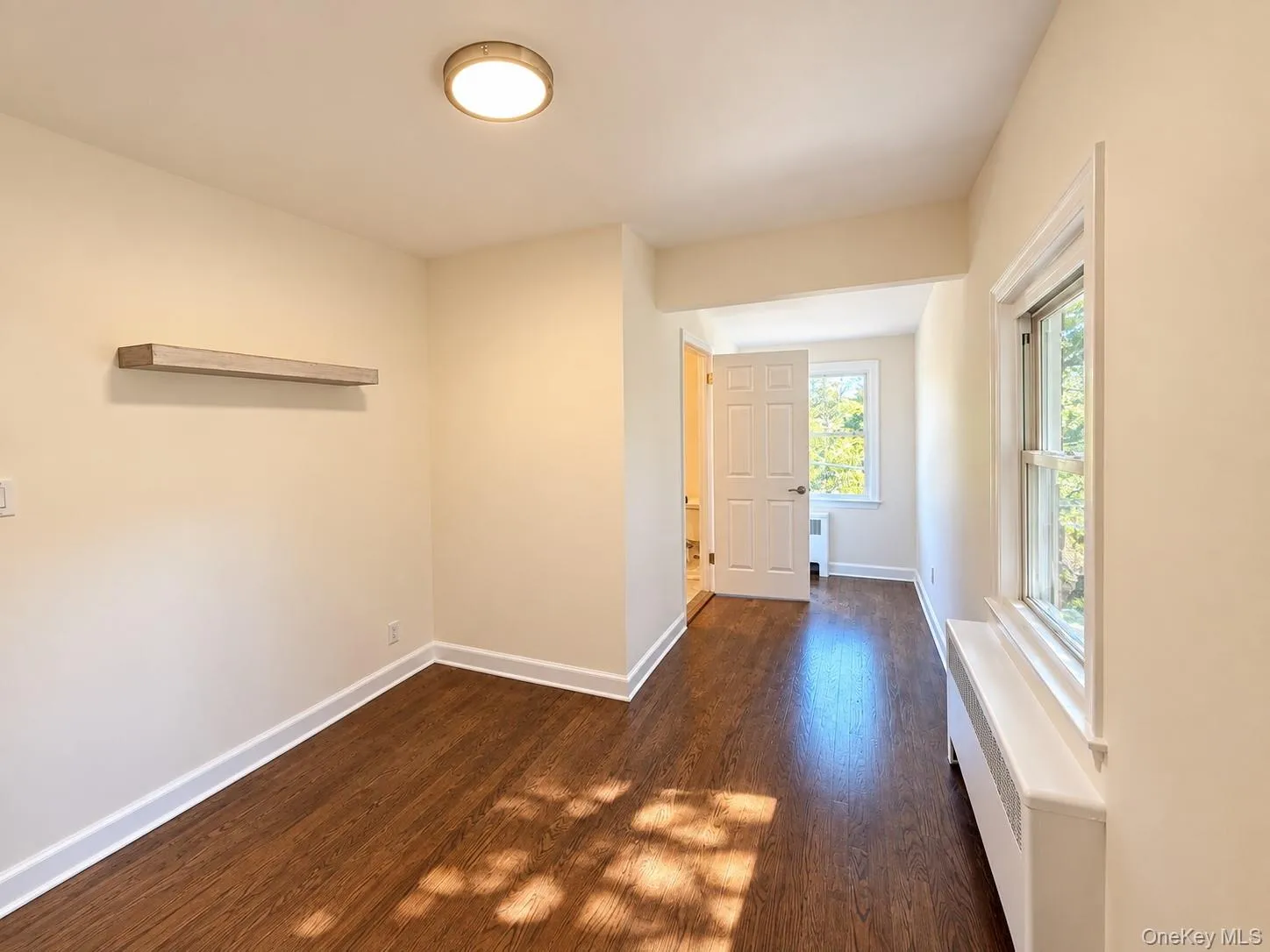 Wood-finish flooring, white trim, recessed lighting, white panel door, and window with natural light, door to a full bathroom. Wood-finish flooring, white trim, recessed lighting, white panel door, and window with natural light, door to a full bathroom.