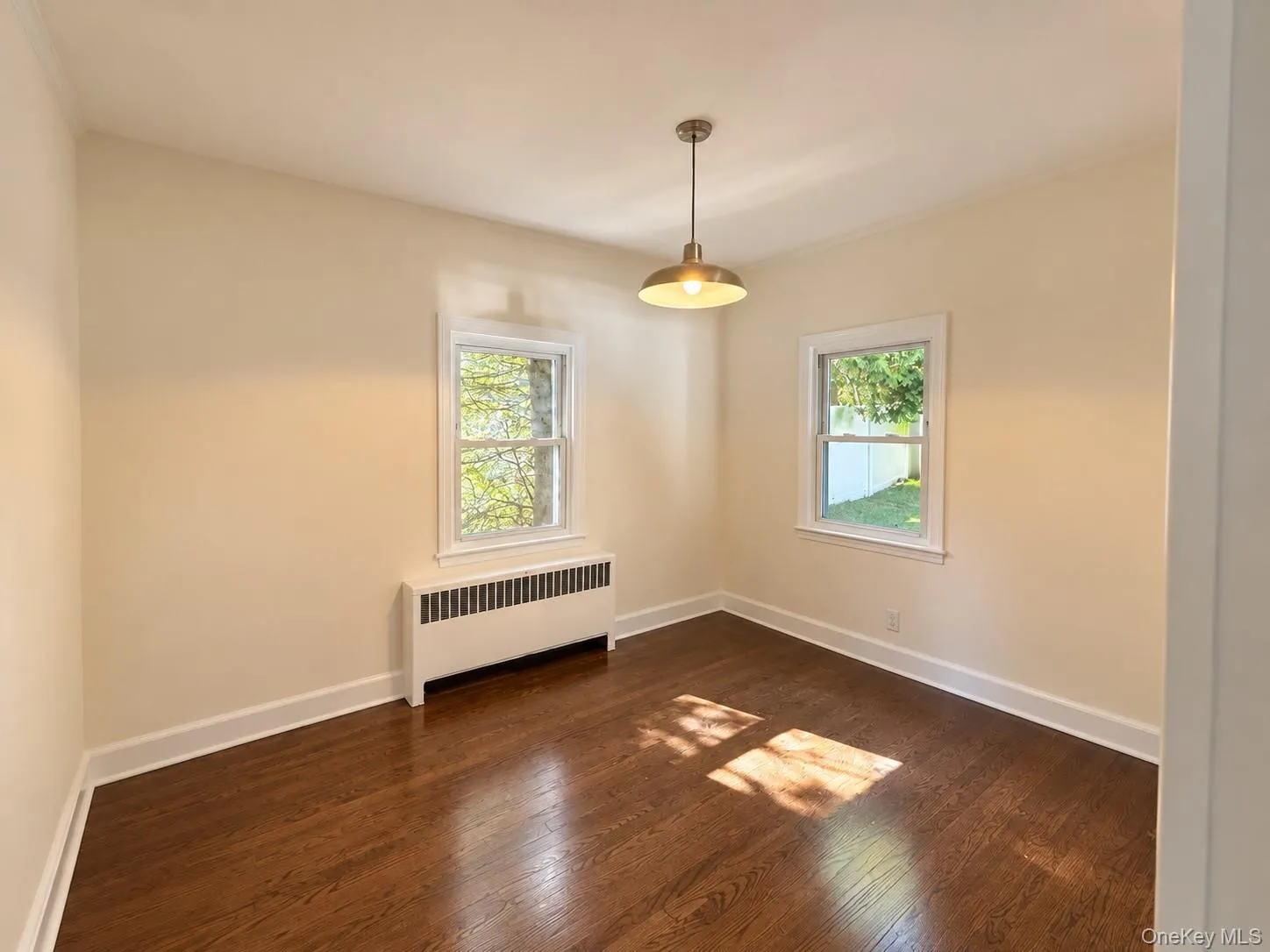 Warm wood-finish flooring, two large windows, a radiator unit, a bronze-finish pendant light fixture, and crown molding Warm wood-finish flooring, two large windows, a radiator unit, a bronze-finish pendant light fixture, and crown molding