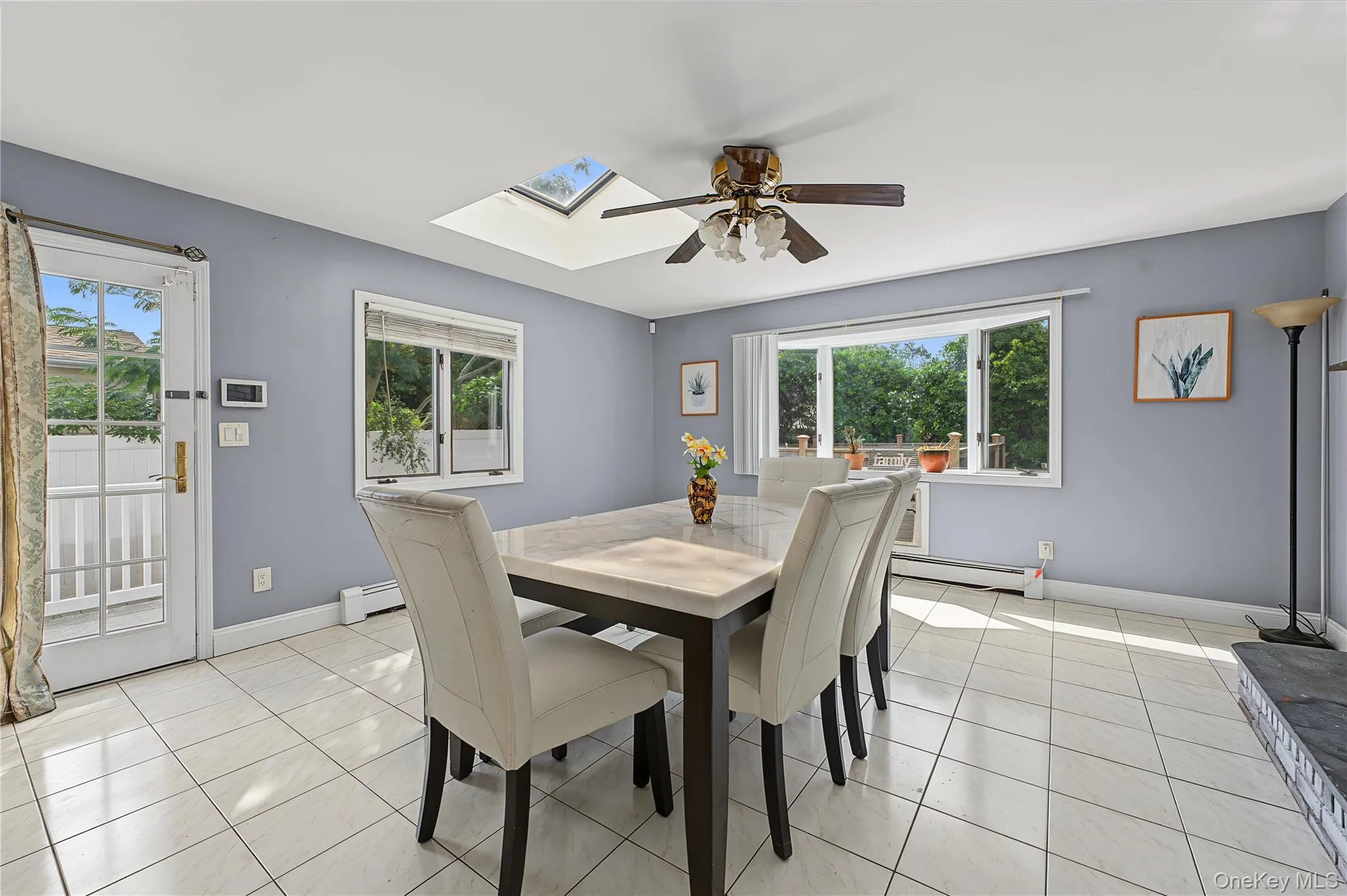 Skylight, ceiling fan, door to the yard and garage access, tiled flooring, and multiple windows including a large bay window and wall mounted air conditioner Skylight, ceiling fan, door to the yard and garage access, tiled flooring, and multiple windows including a large bay window and wall mounted air conditioner