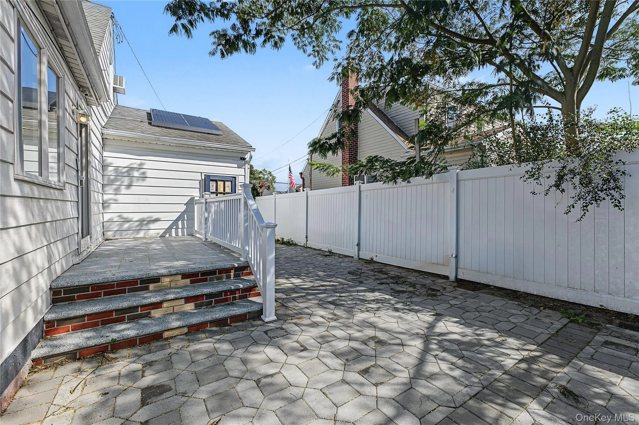 Paver patio area with a white privacy fence and exterior steps featuring brick and stone treads leading to the expansive kitchen/Dining Room Paver patio area with a white privacy fence and exterior steps featuring brick and stone treads leading to the expansive kitchen/Dining Room