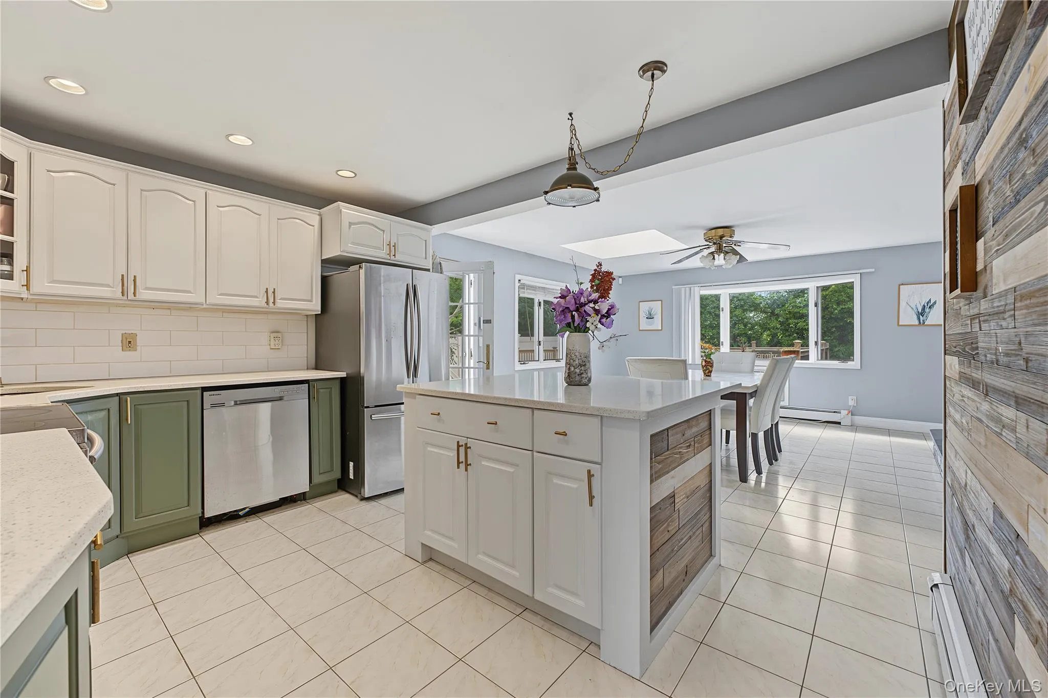 Open Kitchen featuring white shaker-style upper cabinetry, olive green lower cabinetry, stainless steel appliances, a center island that seats 2-3 with wood-finish paneling, and ceramic tile flooring opening up to a huge dining area with a large bay window to the yard and door to the yard allowing easy access to yard and garage Open Kitchen featuring white shaker-style upper cabinetry, olive green lower cabinetry, stainless steel appliances, a center island that seats 2-3 with wood-finish paneling, and ceramic tile flooring opening up to a huge dining area with a large bay window to the yard and door to the yard allowing easy access to yard and garage