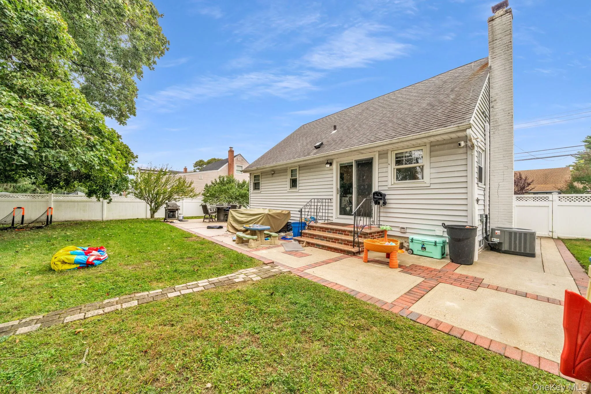 Expansive backyard featuring a manicured lawn, white privacy fencing, a brick and concrete patio. Expansive backyard featuring a manicured lawn, white privacy fencing, a brick and concrete patio.