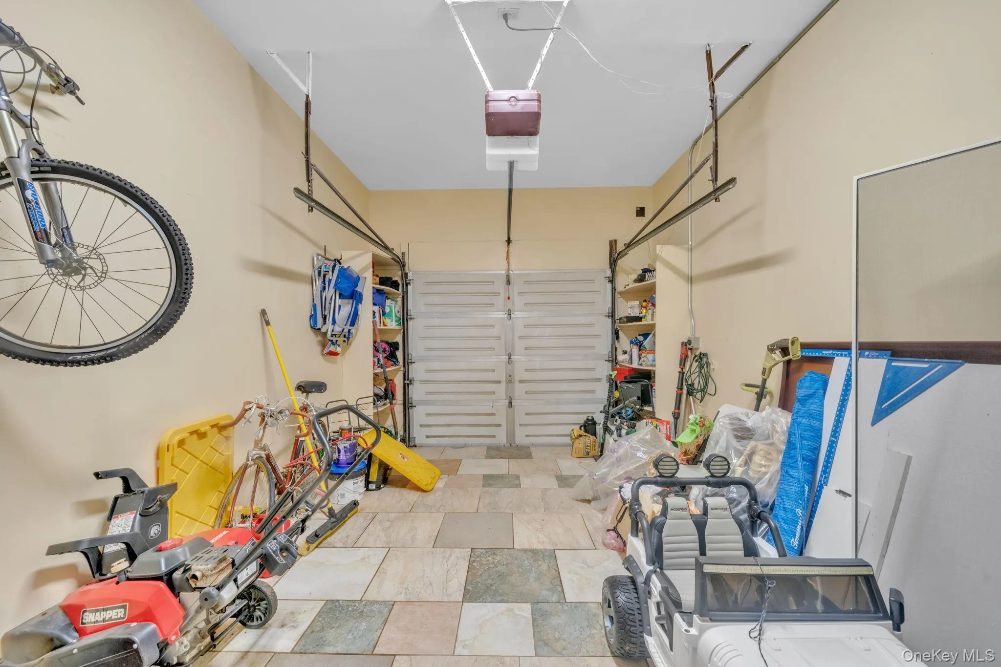 Garage space featuring multi-toned tile flooring, light-toned walls, and a built-in storage rack Garage space featuring multi-toned tile flooring, light-toned walls, and a built-in storage rack