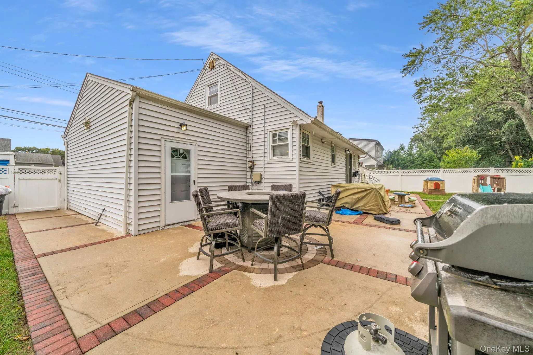Spacious rear patio with concrete and brick accents, white vinyl siding, rear door with decorative glass, and a white fence Spacious rear patio with concrete and brick accents, white vinyl siding, rear door with decorative glass, and a white fence