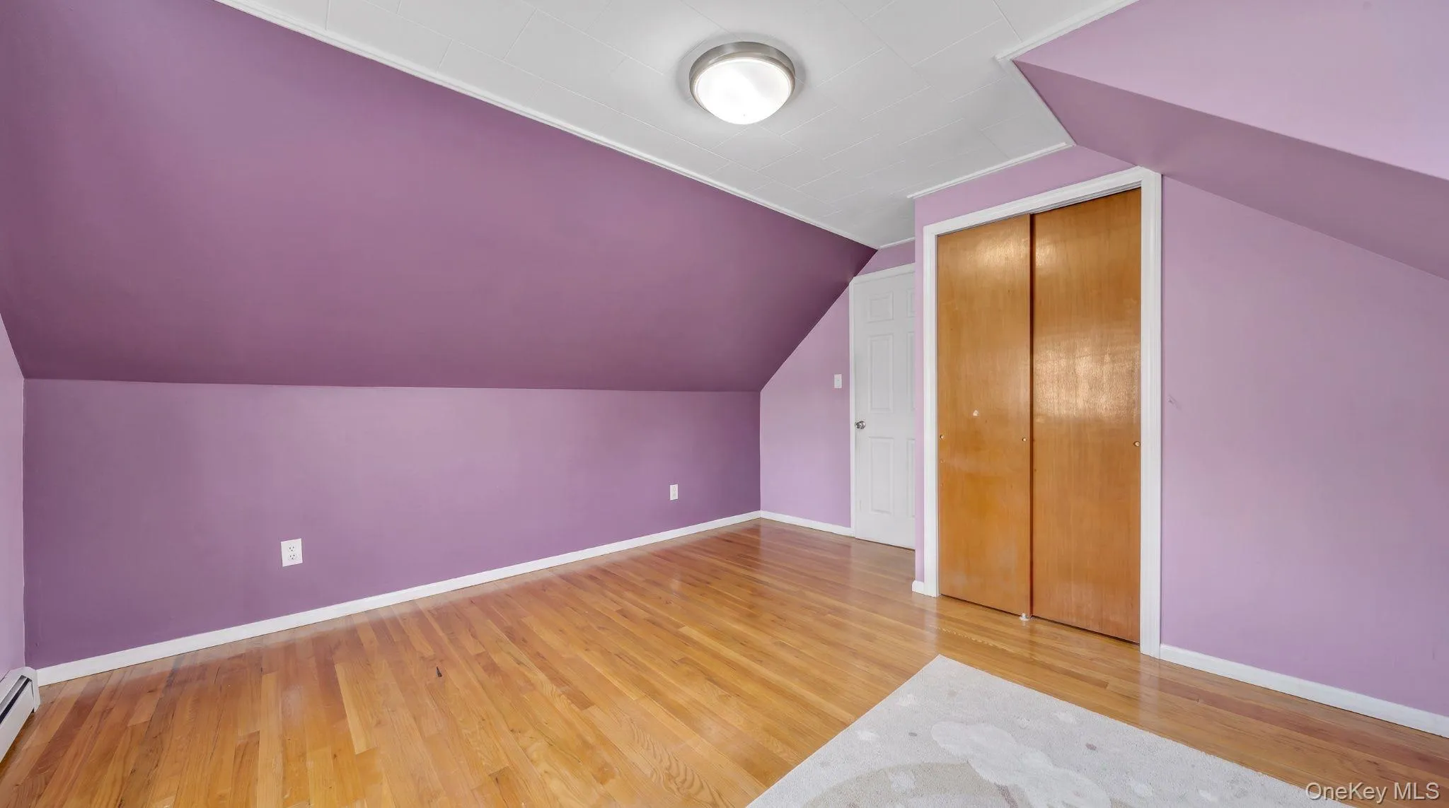 Hardwood flooring, painted walls, built-in closet with bi-fold doors, flush mount ceiling light fixture, and a white door with a round knob Hardwood flooring, painted walls, built-in closet with bi-fold doors, flush mount ceiling light fixture, and a white door with a round knob