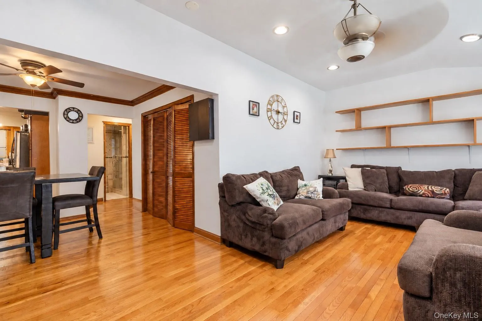 Open living area featuring wood-finish flooring, recessed lighting, ceiling fans, built-in wooden wall shelving, and wooden louvered closet doors Open living area featuring wood-finish flooring, recessed lighting, ceiling fans, built-in wooden wall shelving, and wooden louvered closet doors