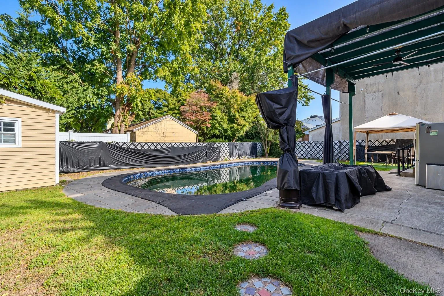 In-ground pool with stone paver surround, covered patio structure, and perimeter lattice fencing In-ground pool with stone paver surround, covered patio structure, and perimeter lattice fencing