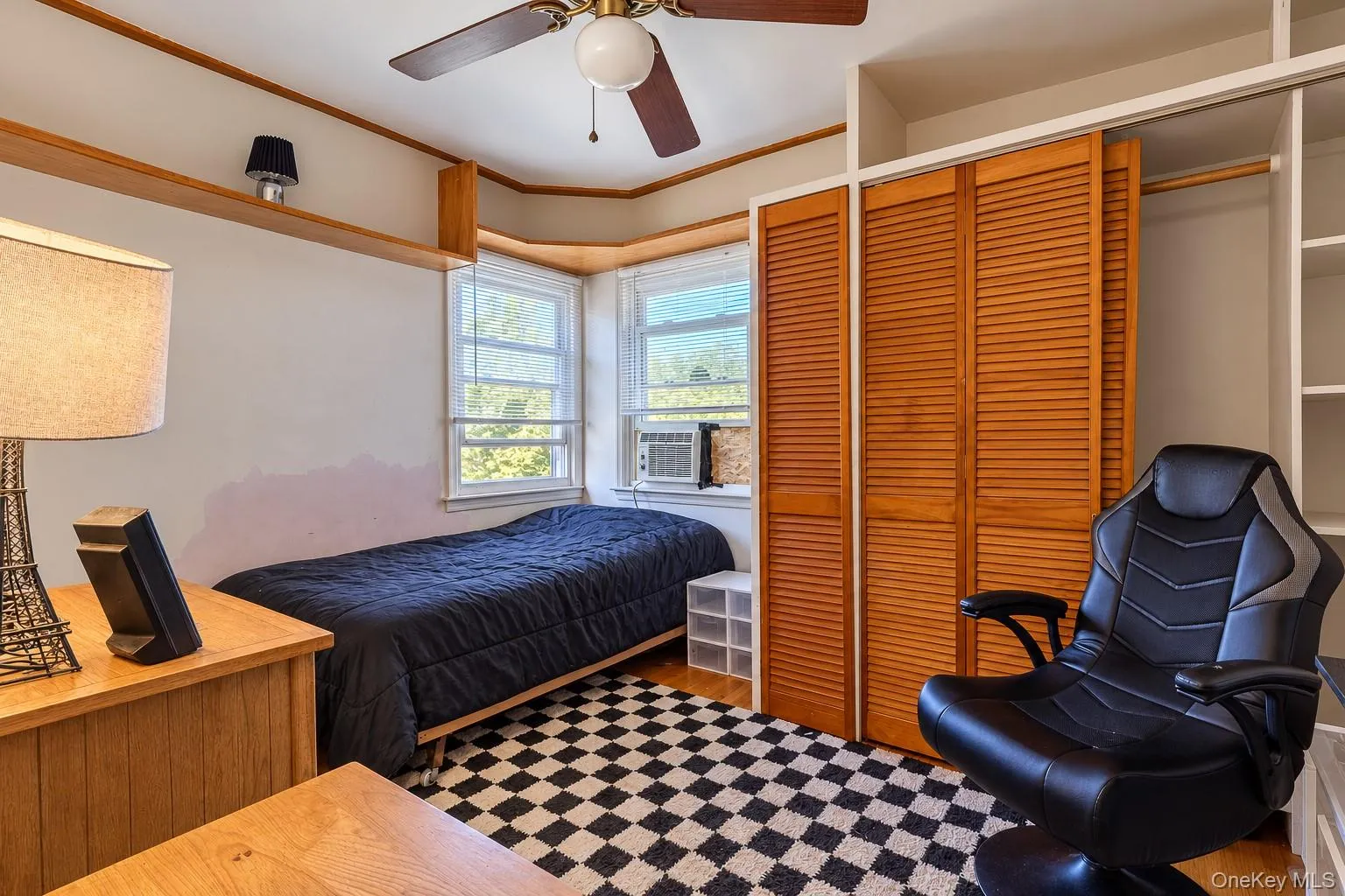 Bay window, built-in wooden shelving, dual-panel louvered closet doors, and a ceiling fan with integrated lighting Bay window, built-in wooden shelving, dual-panel louvered closet doors, and a ceiling fan with integrated lighting