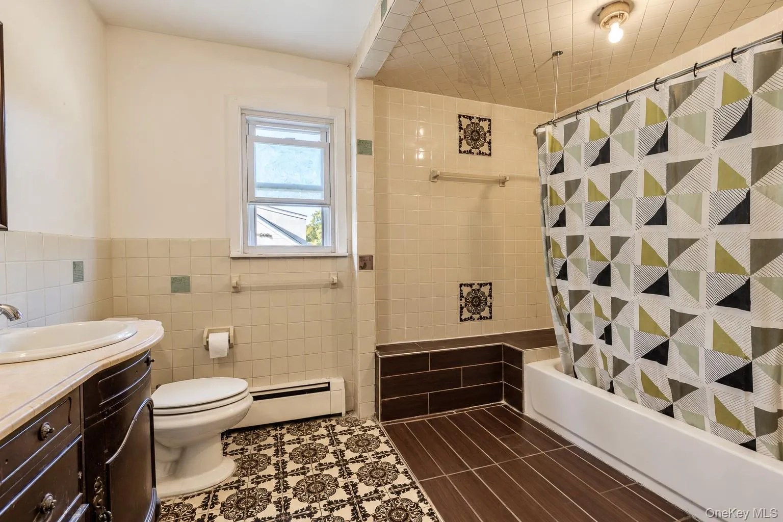 Bathroom featuring a dark wood vanity with an integrated basin, patterned tile flooring, a bathtub surround with decorative tile accents, and a textured tiled ceiling Bathroom featuring a dark wood vanity with an integrated basin, patterned tile flooring, a bathtub surround with decorative tile accents, and a textured tiled ceiling