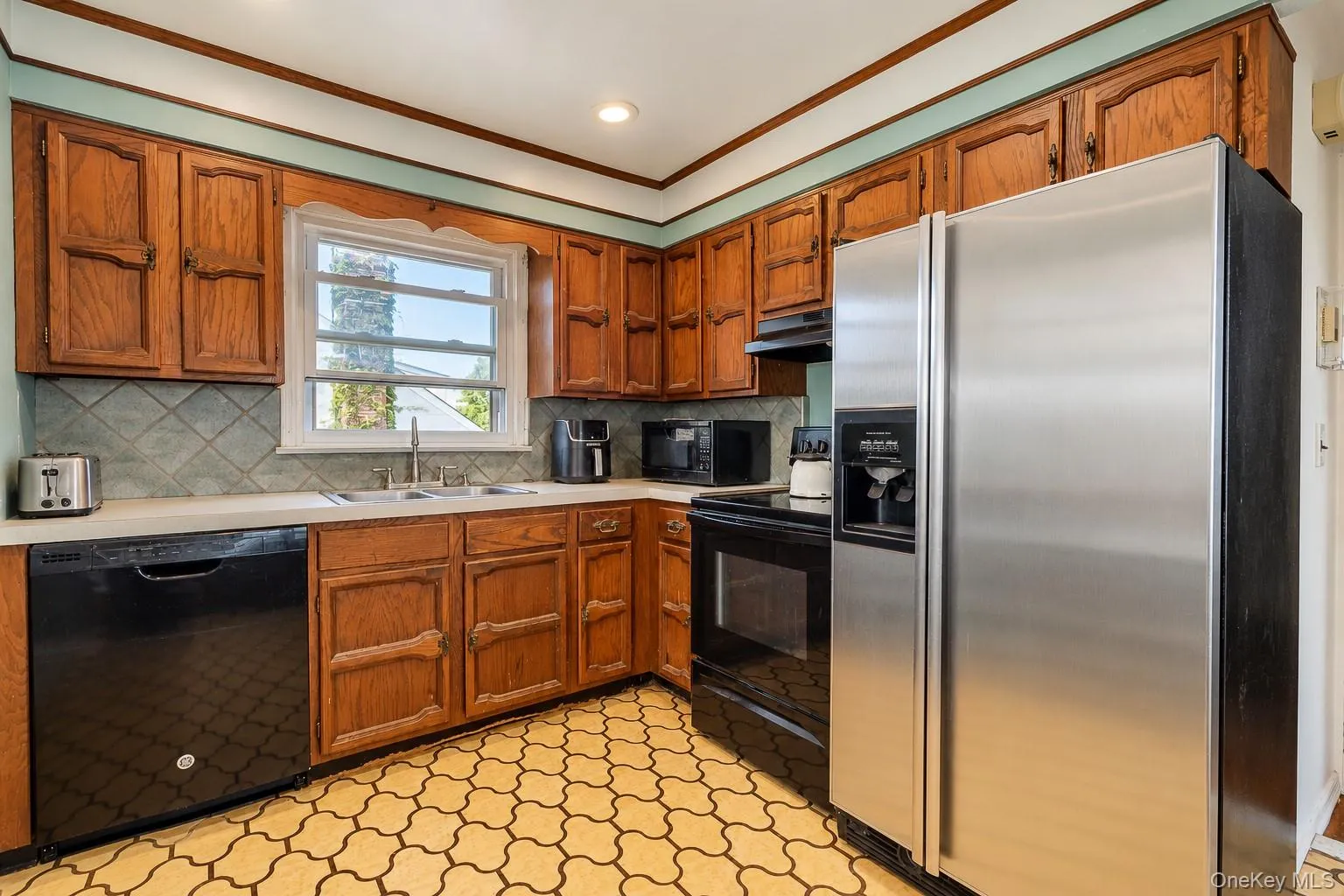 Kitchen featuring stained wood cabinetry, stainless steel refrigerator, patterned tile flooring, and a tiled backsplash Kitchen featuring stained wood cabinetry, stainless steel refrigerator, patterned tile flooring, and a tiled backsplash