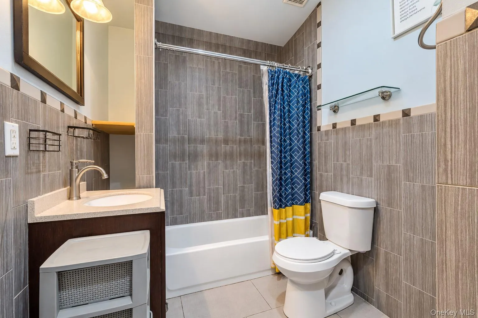 Bathroom featuring stone-finish wall tiling with mosaic accents, a built-in vanity with a stone countertop, an integrated oval sink, and a combination bathtub and shower enclosure with a stainless steel faucet Bathroom featuring stone-finish wall tiling with mosaic accents, a built-in vanity with a stone countertop, an integrated oval sink, and a combination bathtub and shower enclosure with a stainless steel faucet