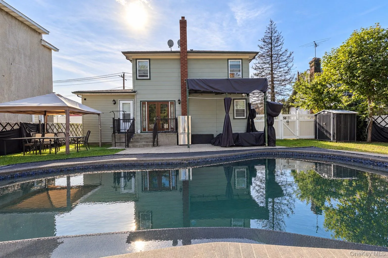 Exterior backyard featuring an in-ground swimming pool, concrete patio, red brick chimney, and white vinyl privacy fencing Exterior backyard featuring an in-ground swimming pool, concrete patio, red brick chimney, and white vinyl privacy fencing