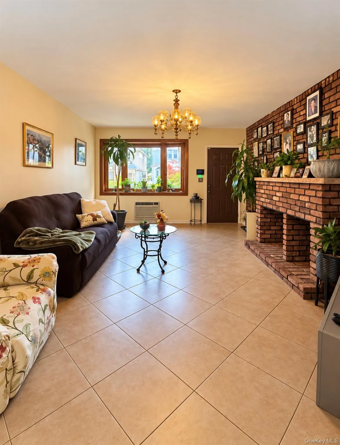 Spacious living area featuring tile flooring, a prominent brick-clad fireplace, and a decorative chandelier Spacious living area featuring tile flooring, a prominent brick-clad fireplace, and a decorative chandelier