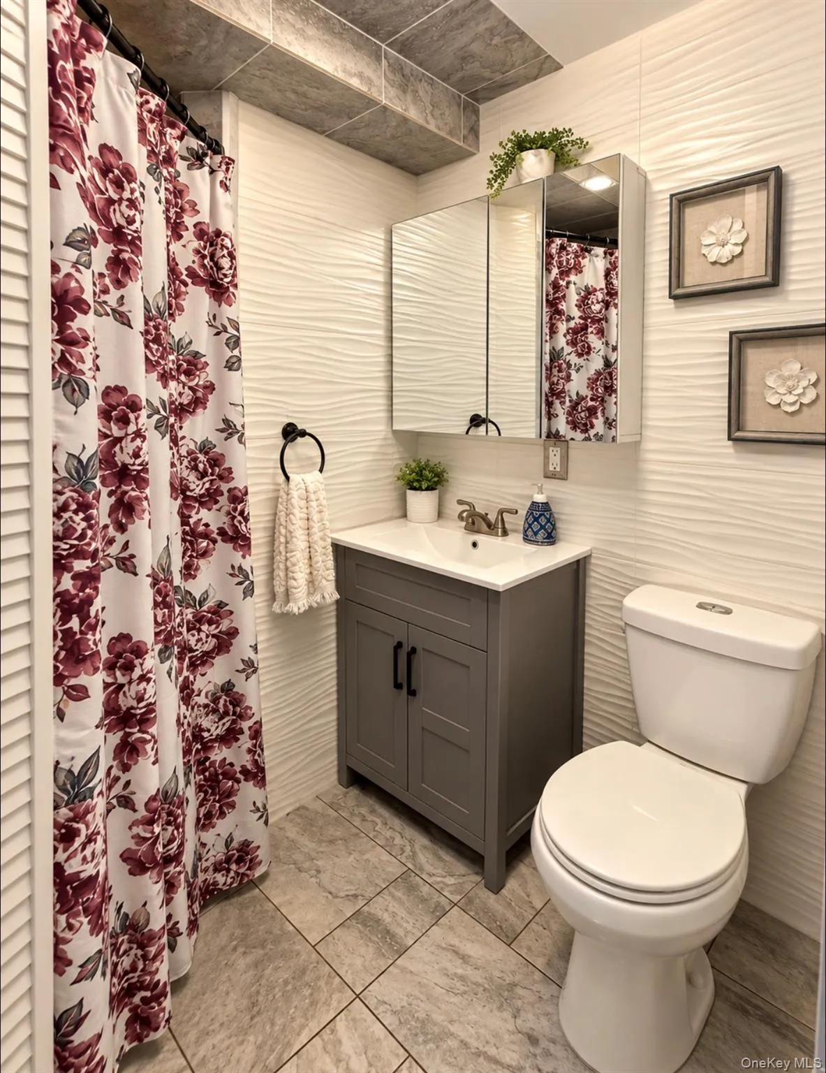 Wavy-textured wall tile, gray vanity with double cabinet doors, integrated sink, mirrored medicine cabinet, and large-format tile flooring Wavy-textured wall tile, gray vanity with double cabinet doors, integrated sink, mirrored medicine cabinet, and large-format tile flooring