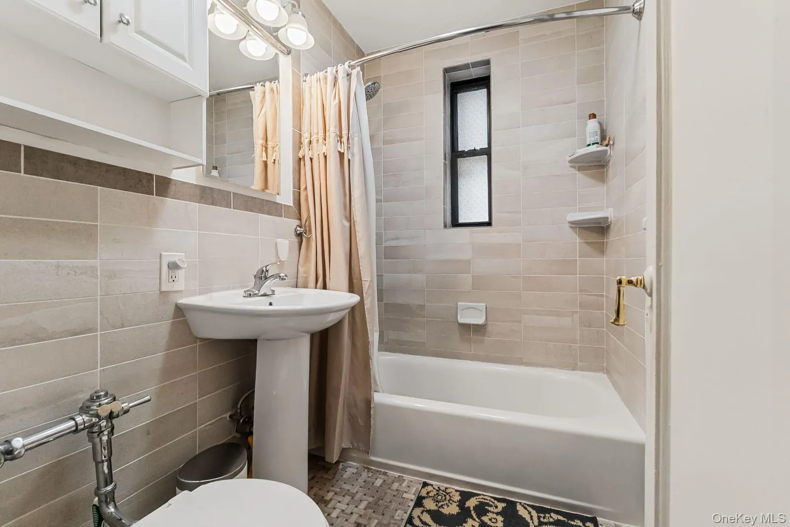 Pedestal sink, wall-mounted light fixture, white cabinetry, tiled walls, and a built-in bathtub Pedestal sink, wall-mounted light fixture, white cabinetry, tiled walls, and a built-in bathtub