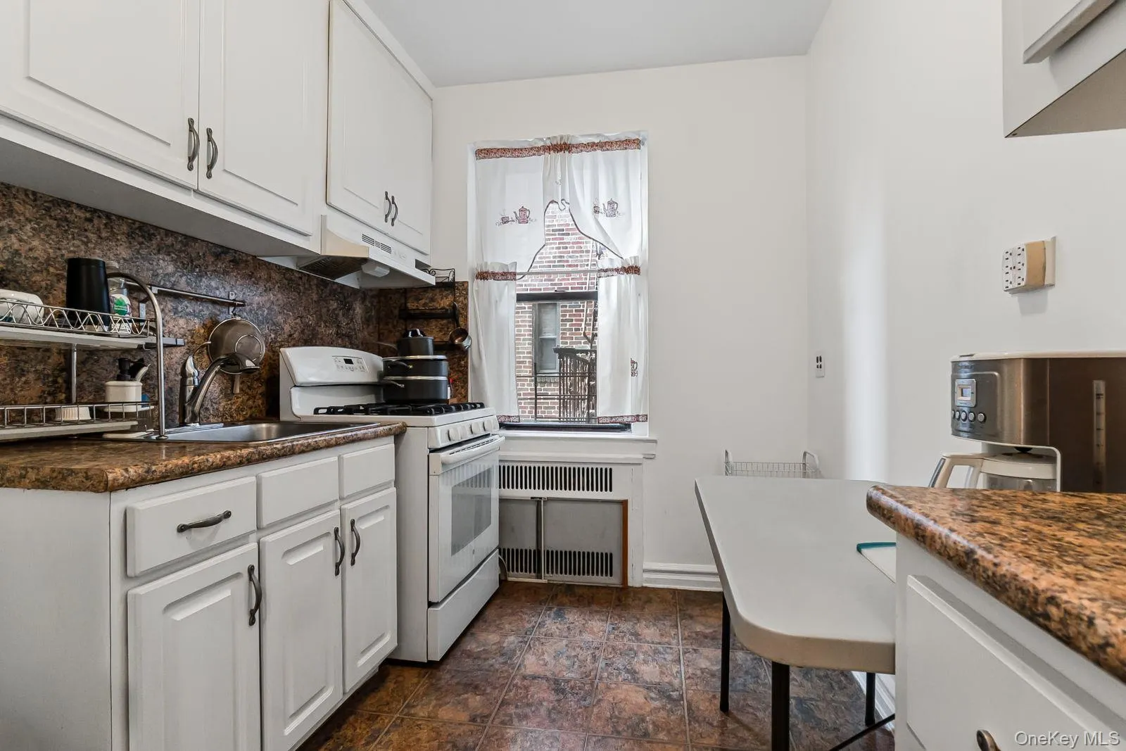 Kitchen featuring white cabinetry, brown patterned countertops, tile backsplash, and a window Kitchen featuring white cabinetry, brown patterned countertops, tile backsplash, and a window