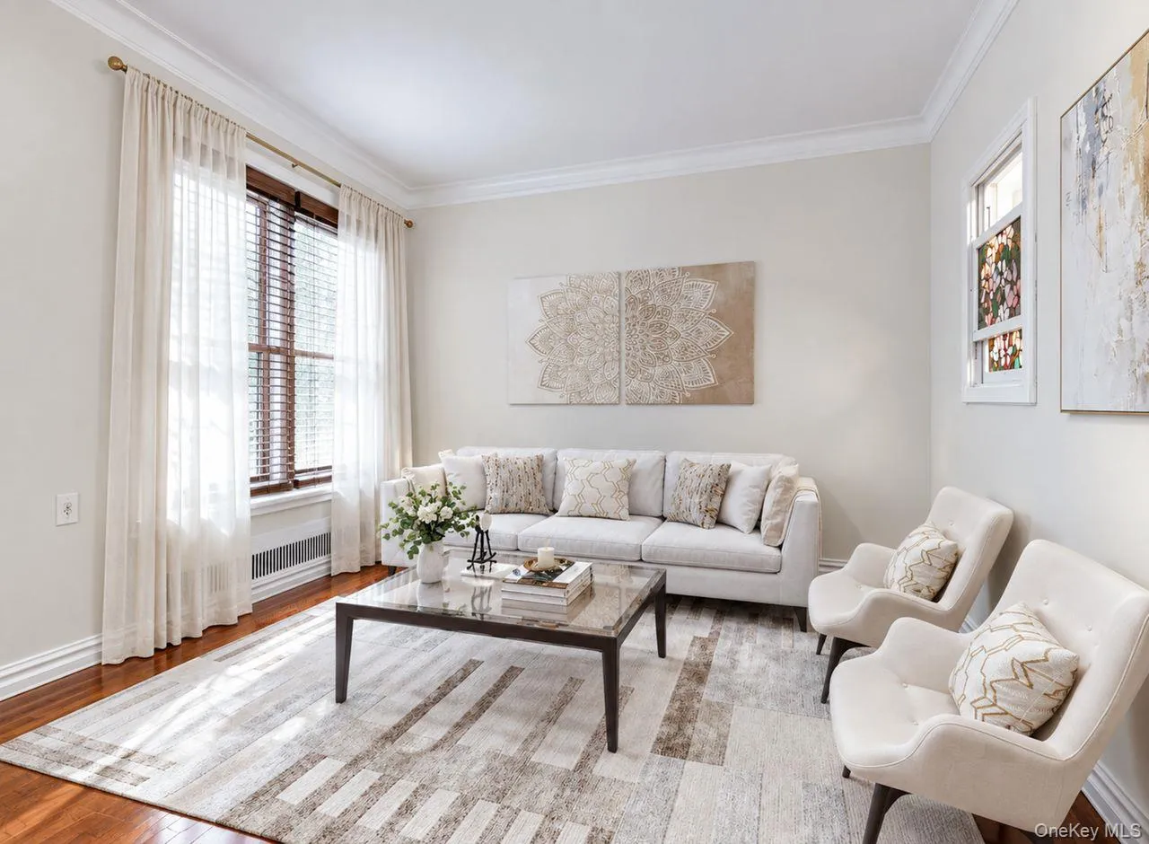 Hardwood flooring, crown molding, large window with wood blinds, white walls, and a built-in radiator Hardwood flooring, crown molding, large window with wood blinds, white walls, and a built-in radiator