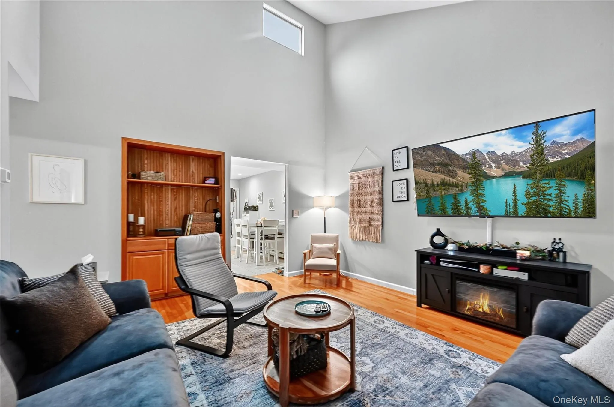Living room featuring a towering ceiling, light wood-type flooring, and a glass covered fireplace Living room featuring a towering ceiling, light wood-type flooring, and a glass covered fireplace