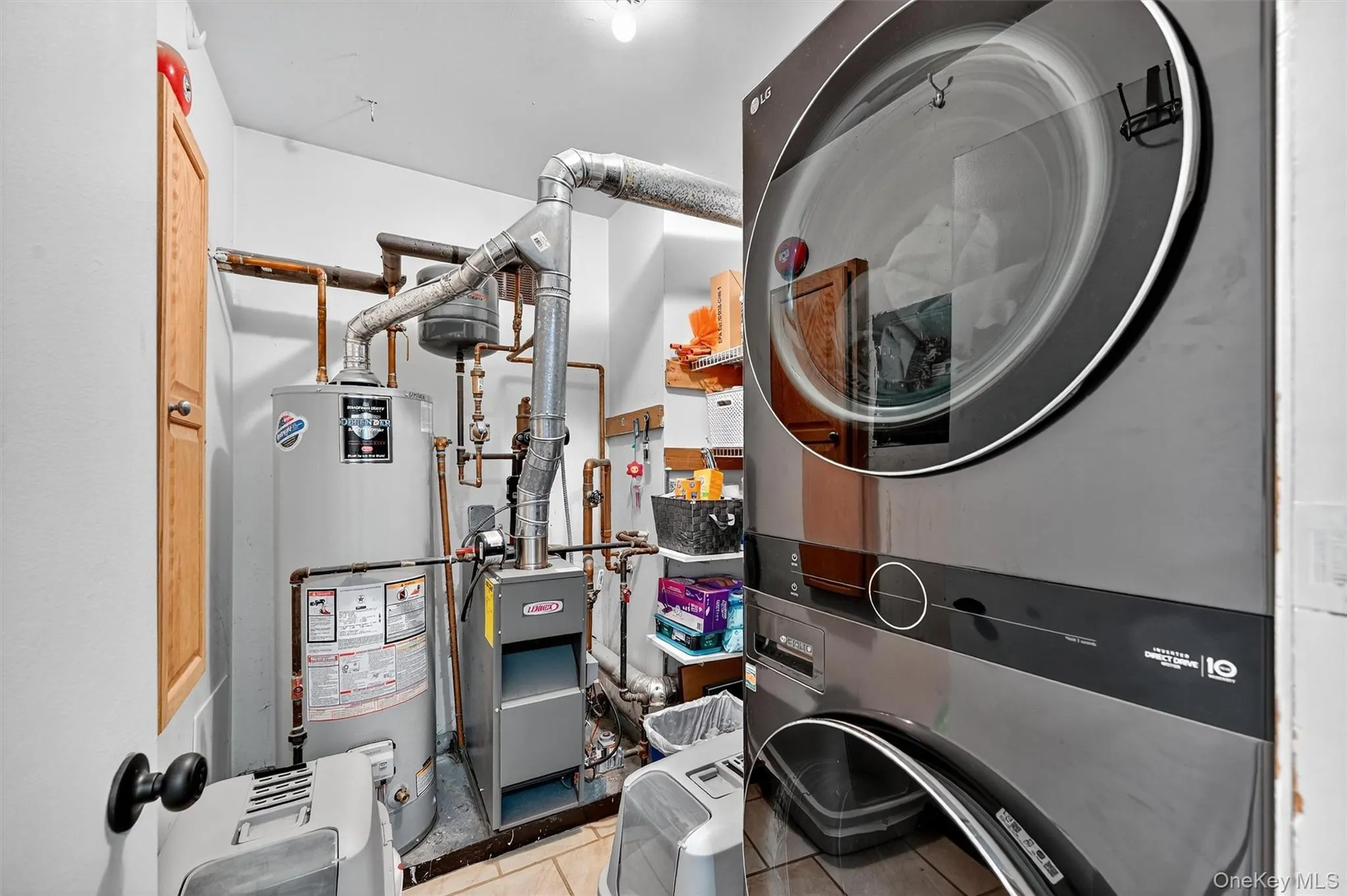 Laundry area with light tile patterned flooring, water heater, stacked washer / dryer, and a heating unit Laundry area with light tile patterned flooring, water heater, stacked washer / dryer, and a heating unit