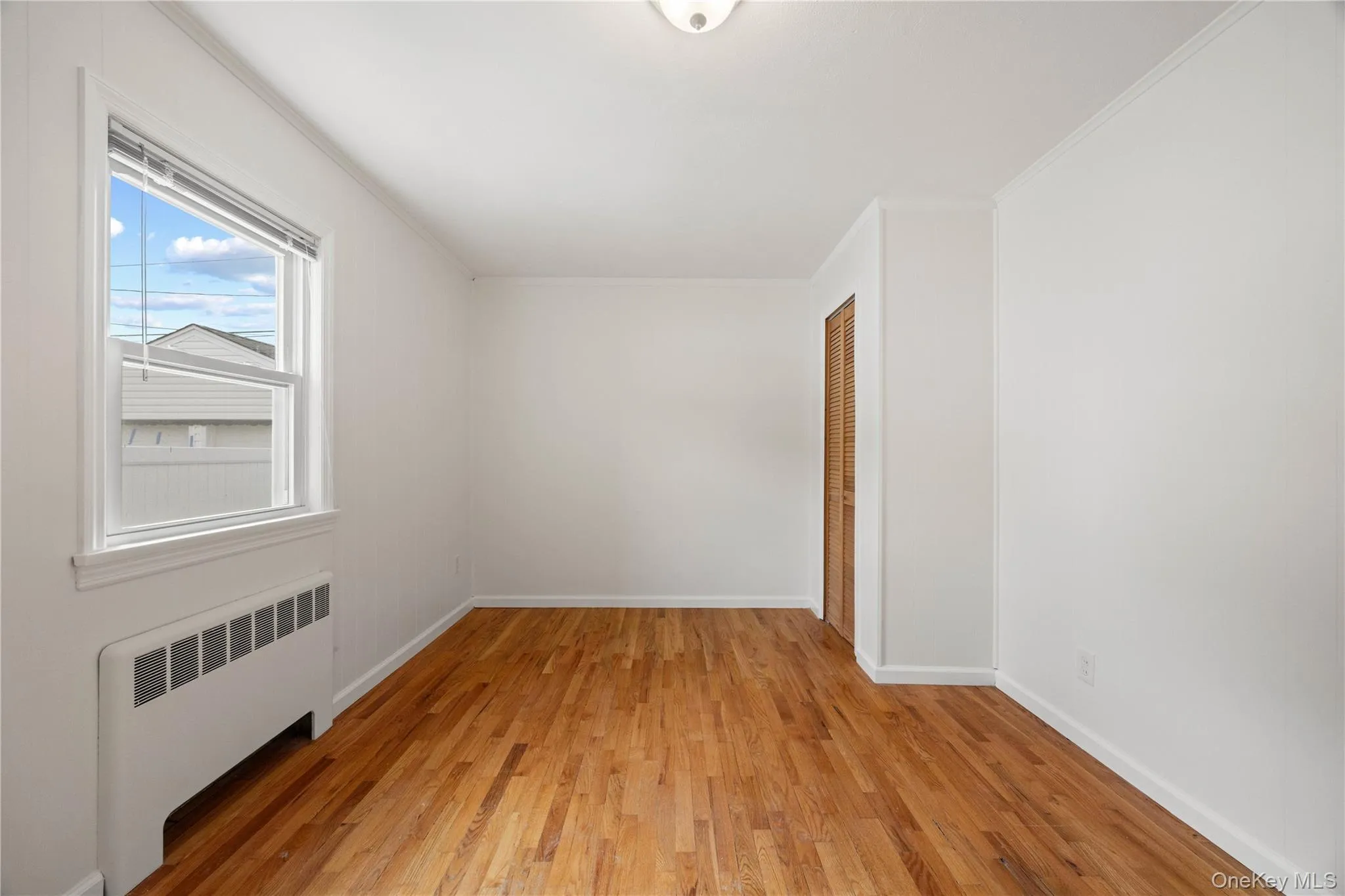 Hardwood flooring, painted white walls, white window trim, white crown molding, and a wood-finish bi-fold door Hardwood flooring, painted white walls, white window trim, white crown molding, and a wood-finish bi-fold door