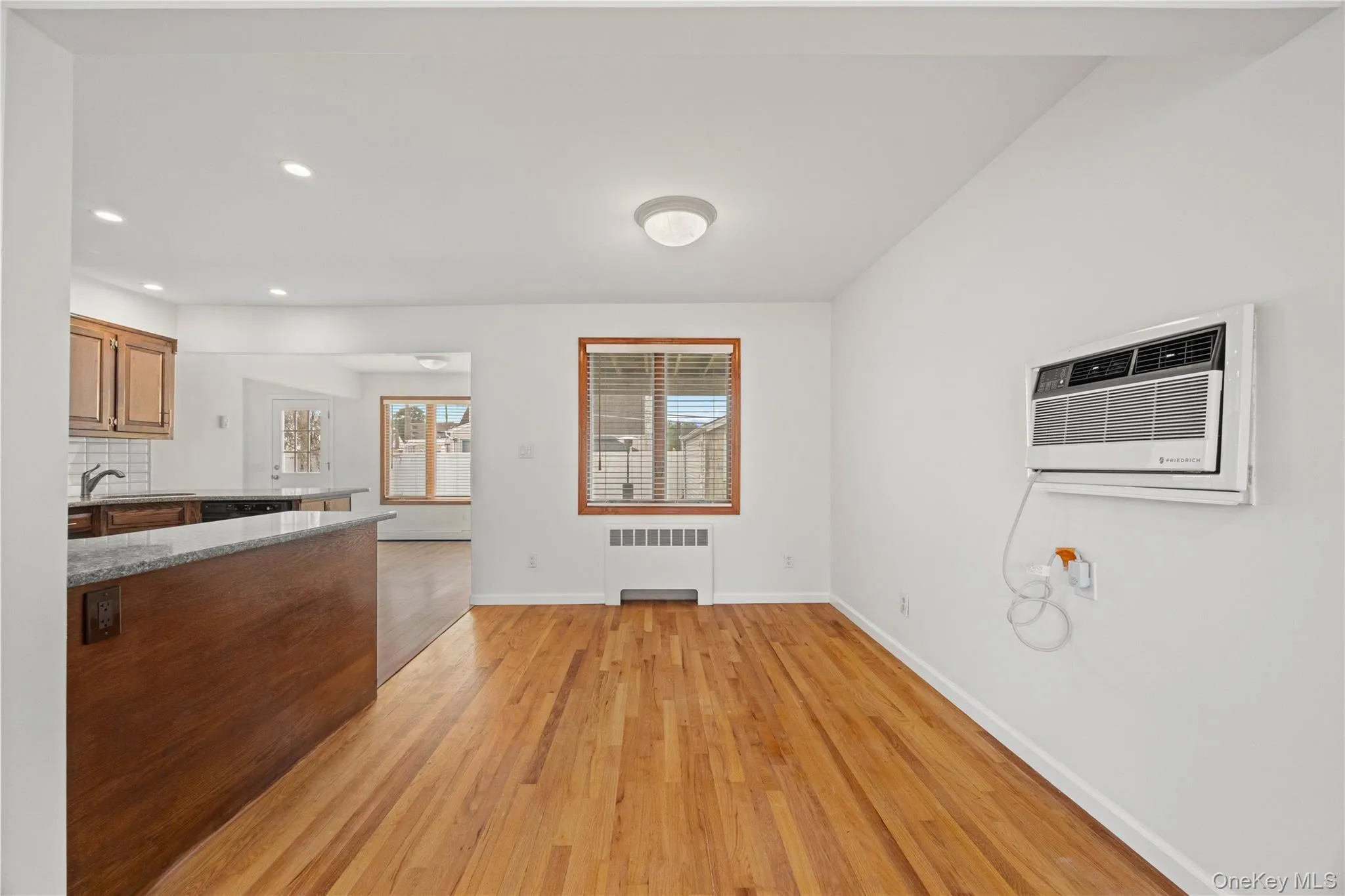 Hardwood flooring, recessed lighting, kitchen peninsula with granite countertop, wood cabinetry, and a wall-mounted air conditioning unit Hardwood flooring, recessed lighting, kitchen peninsula with granite countertop, wood cabinetry, and a wall-mounted air conditioning unit
