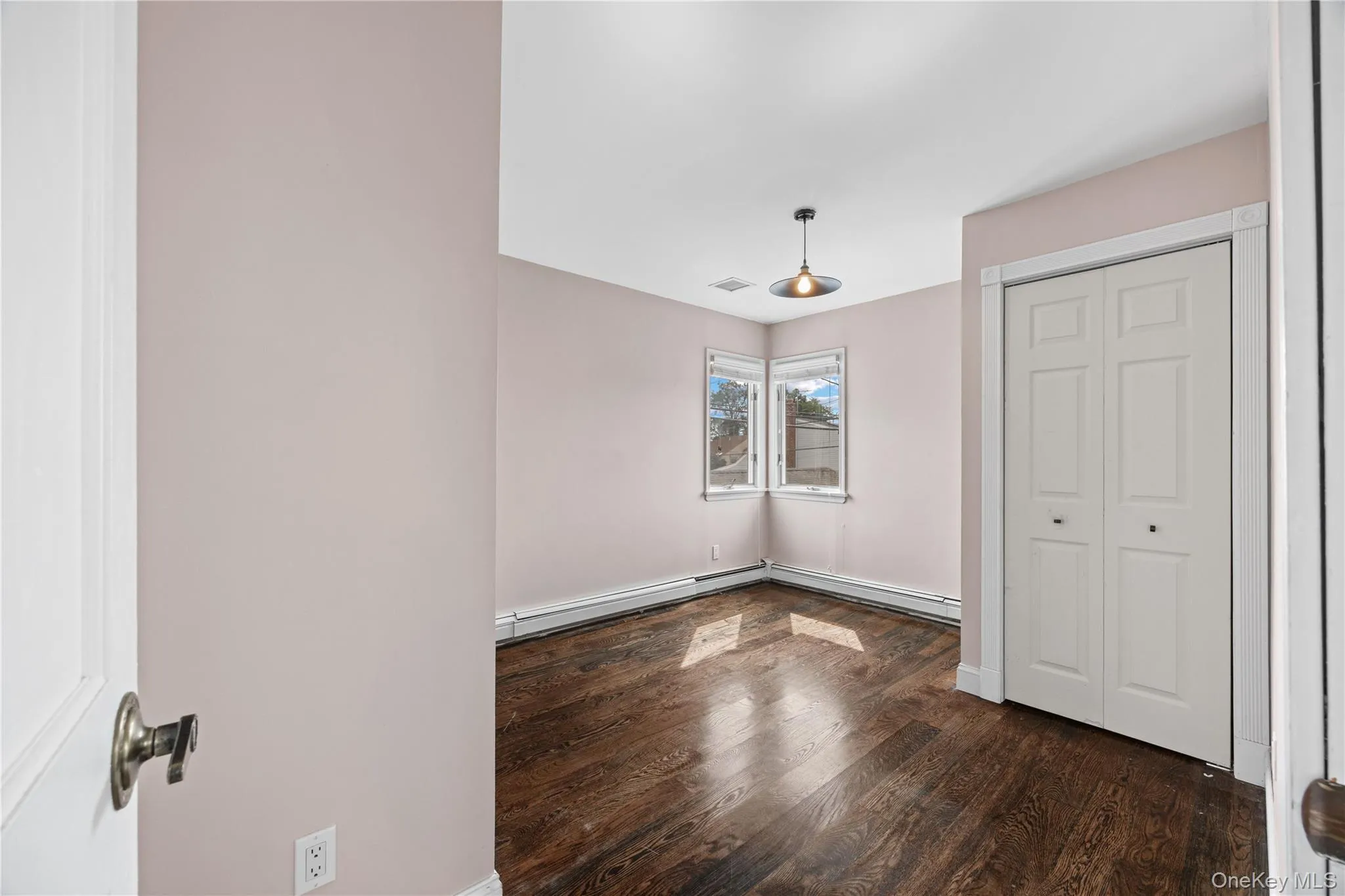 Hardwood flooring with a corner window, bi-fold closet doors, and a ceiling-mounted light fixture Hardwood flooring with a corner window, bi-fold closet doors, and a ceiling-mounted light fixture