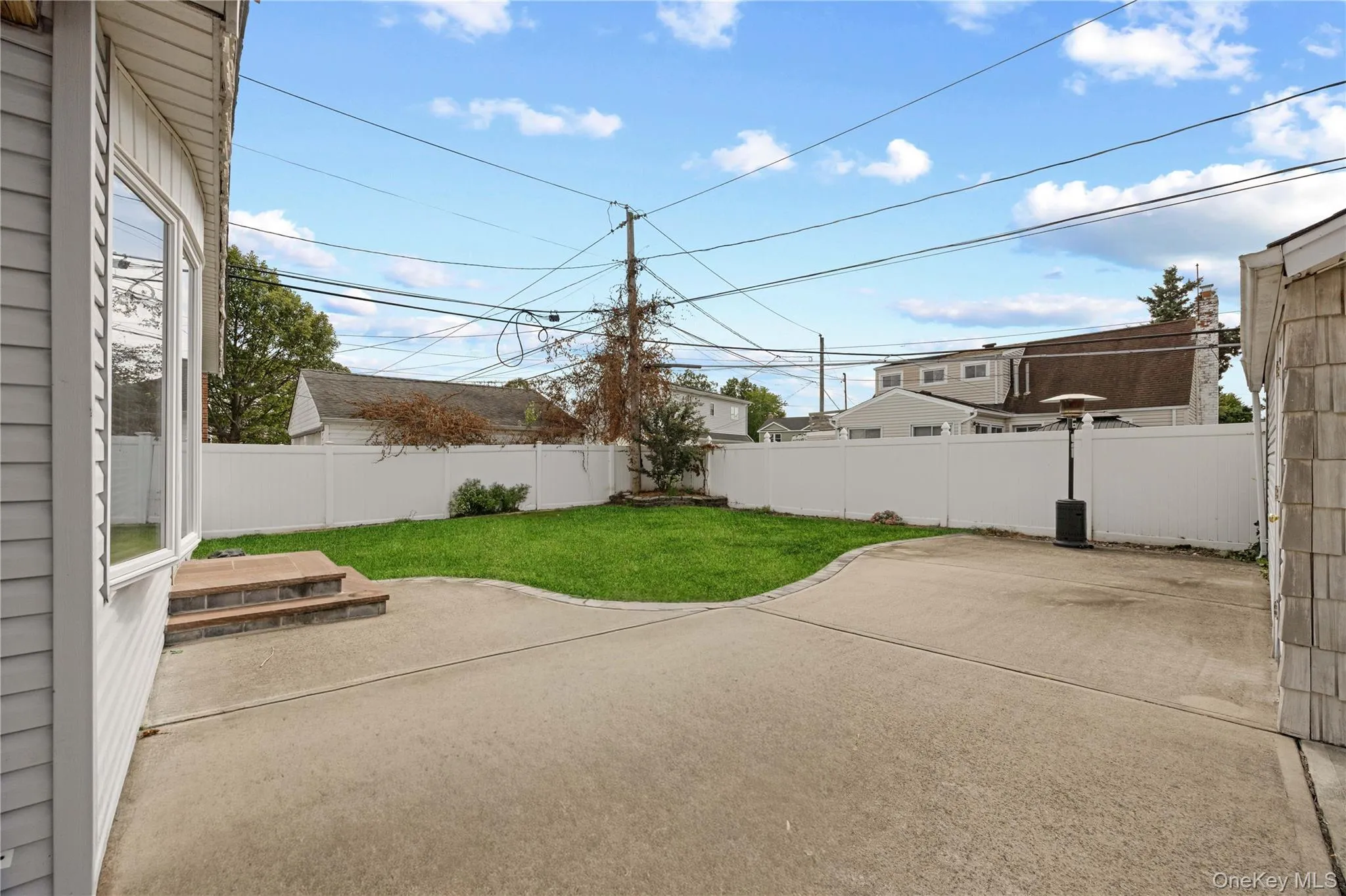Concrete patio area with a manicured lawn section and white privacy fencing Concrete patio area with a manicured lawn section and white privacy fencing