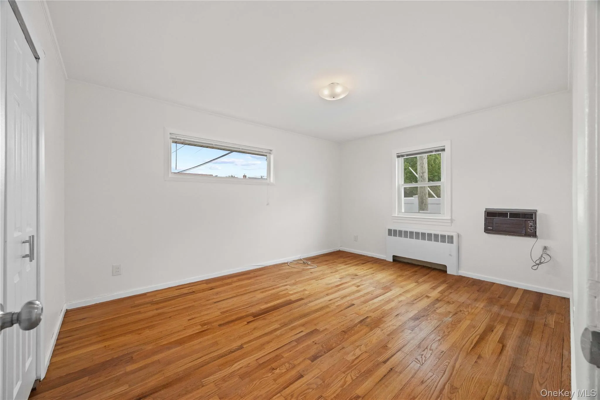 Hardwood flooring, white painted walls, two windows, and a flush mount ceiling light Hardwood flooring, white painted walls, two windows, and a flush mount ceiling light