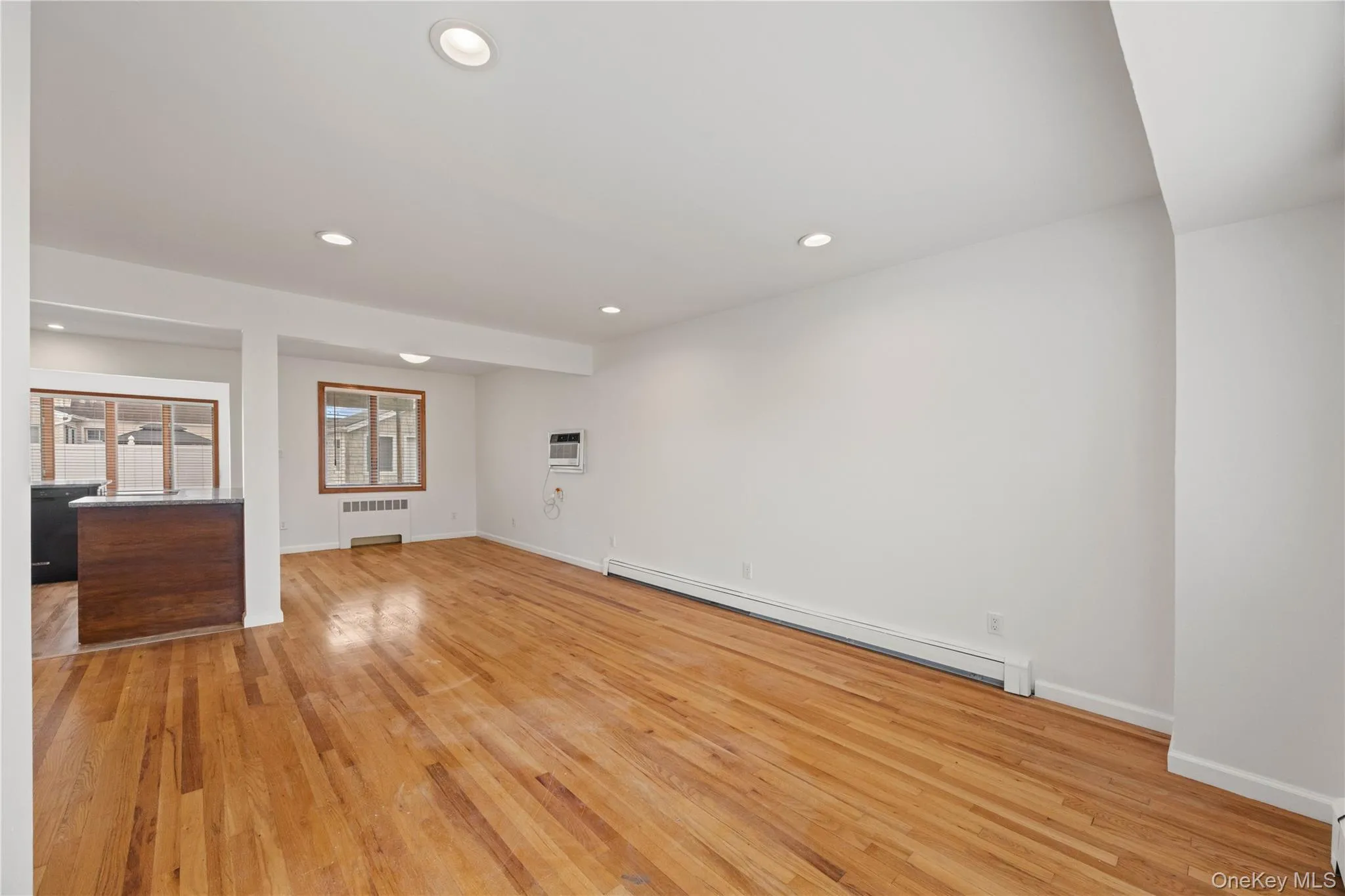Recessed ceiling lighting, wood-finish flooring, and a built-in breakfast bar with a dark countertop Recessed ceiling lighting, wood-finish flooring, and a built-in breakfast bar with a dark countertop