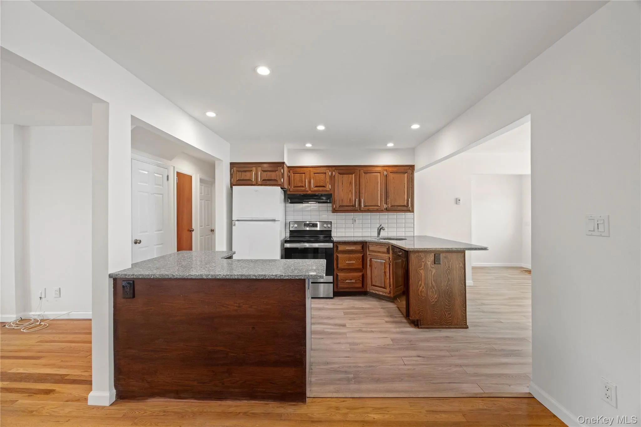 Kitchen featuring wood cabinetry, stainless steel range, white subway tile backsplash, and light-toned wood-finish flooring Kitchen featuring wood cabinetry, stainless steel range, white subway tile backsplash, and light-toned wood-finish flooring