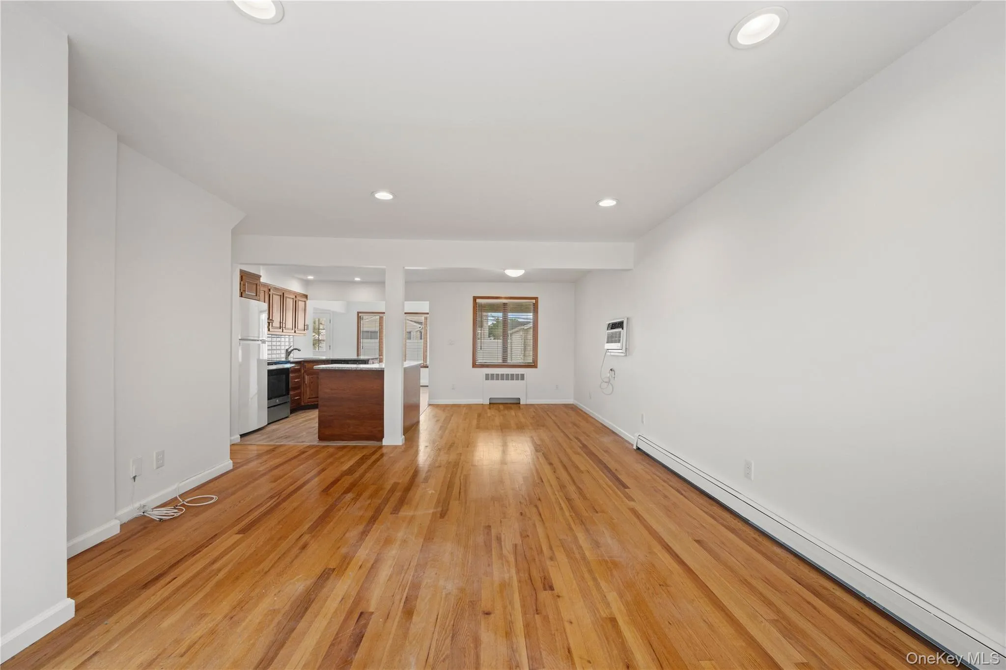 Wood-finish flooring throughout, recessed ceiling lighting, and a kitchen with wood cabinetry and a white refrigerator Wood-finish flooring throughout, recessed ceiling lighting, and a kitchen with wood cabinetry and a white refrigerator