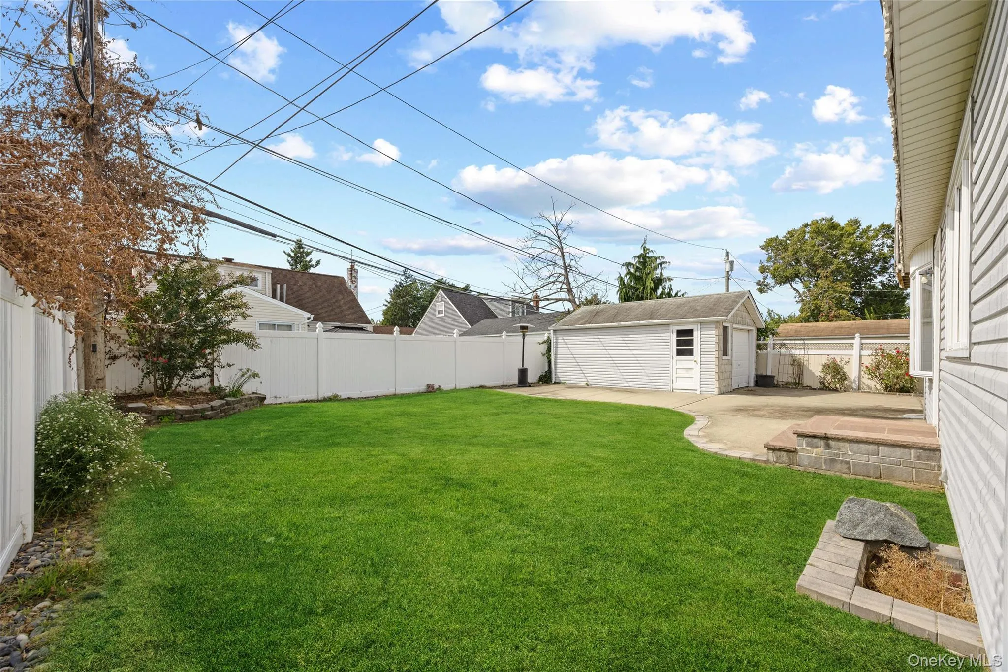 Expansive lawn with a white privacy fence, detached garage, concrete patio, and stone landscape borders Expansive lawn with a white privacy fence, detached garage, concrete patio, and stone landscape borders