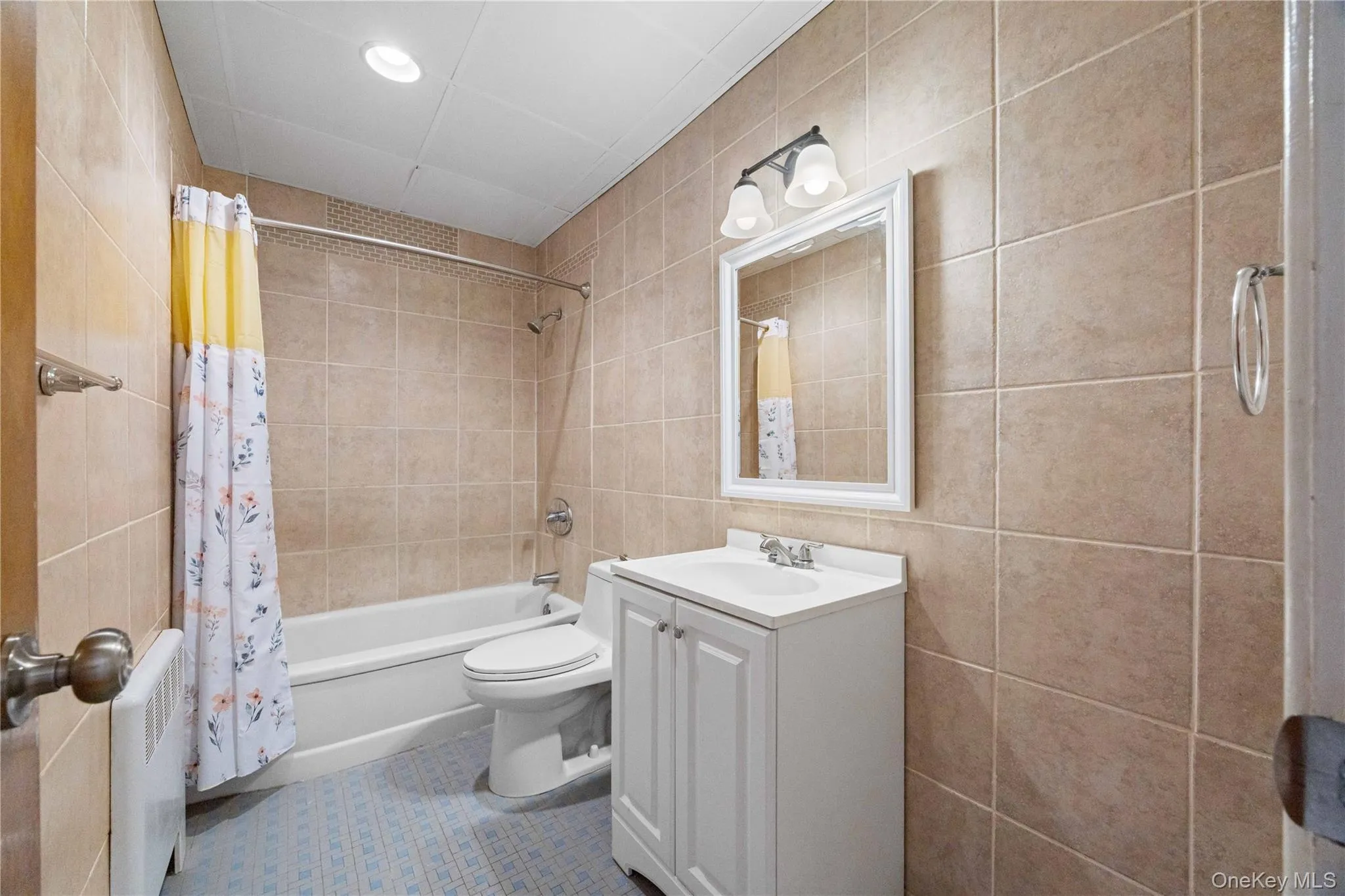 Full tile surround, white vanity, integrated sink, mirrored cabinet, and recessed ceiling lighting Full tile surround, white vanity, integrated sink, mirrored cabinet, and recessed ceiling lighting