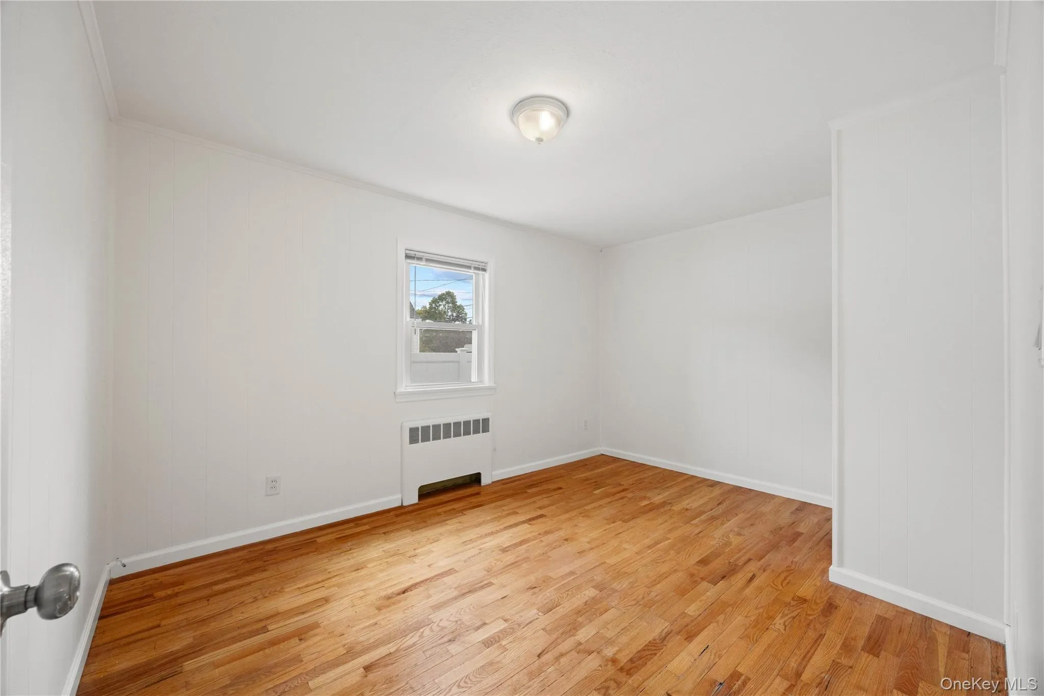 Wood-finish flooring, white painted walls, single window, baseboard heating unit, and ceiling-mounted light fixture Wood-finish flooring, white painted walls, single window, baseboard heating unit, and ceiling-mounted light fixture