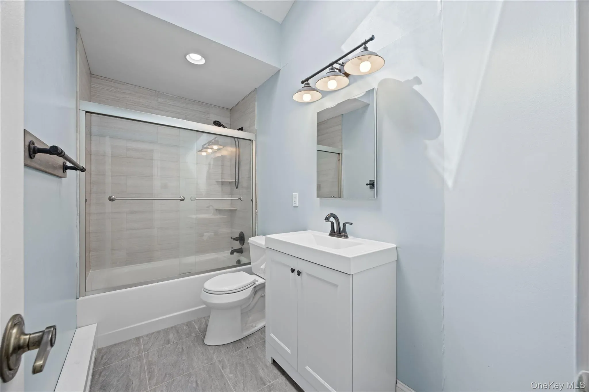 Sliding glass shower enclosure, white vanity with integrated sink, rectangular mirror, three-light vanity fixture, and recessed ceiling lighting Sliding glass shower enclosure, white vanity with integrated sink, rectangular mirror, three-light vanity fixture, and recessed ceiling lighting