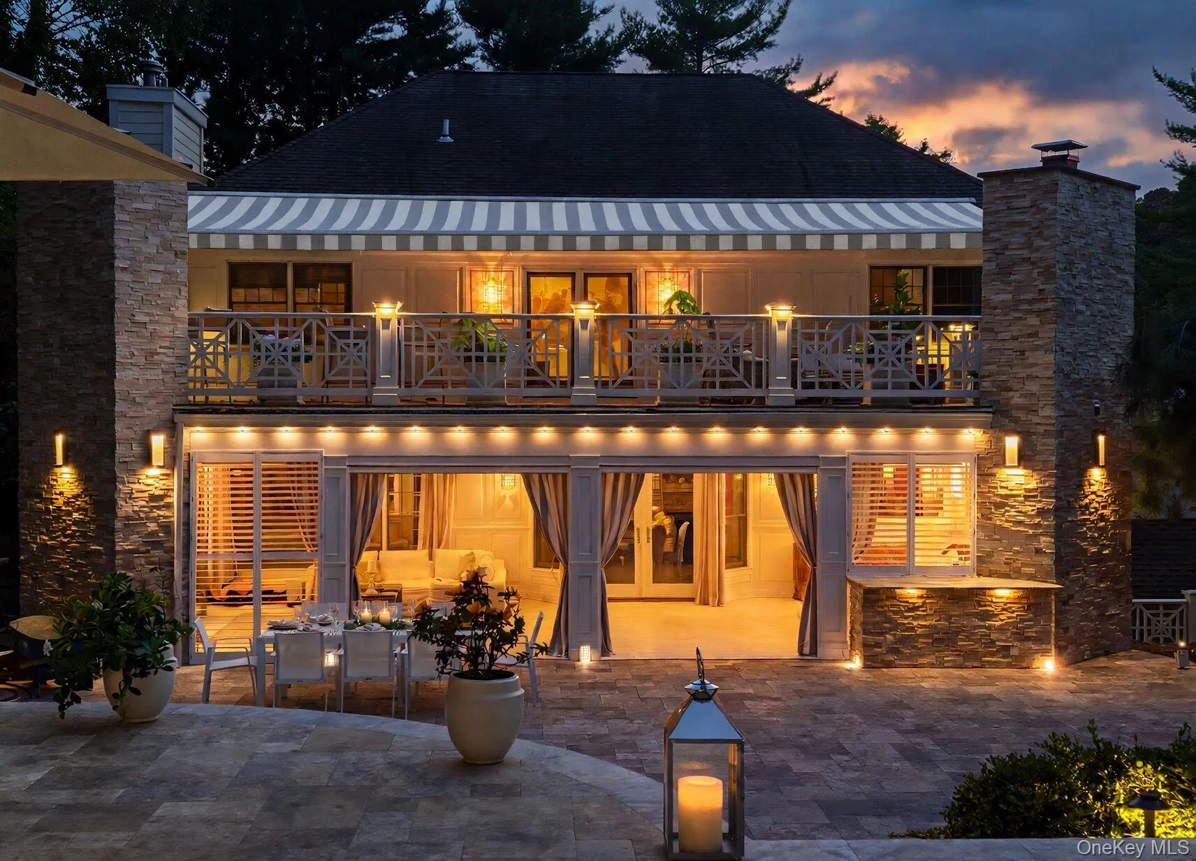 Multi-level exterior with a stone-clad chimney and columns, featuring a second-story balcony with decorative railing, and a retractable striped awning Multi-level exterior with a stone-clad chimney and columns, featuring a second-story balcony with decorative railing, and a retractable striped awning