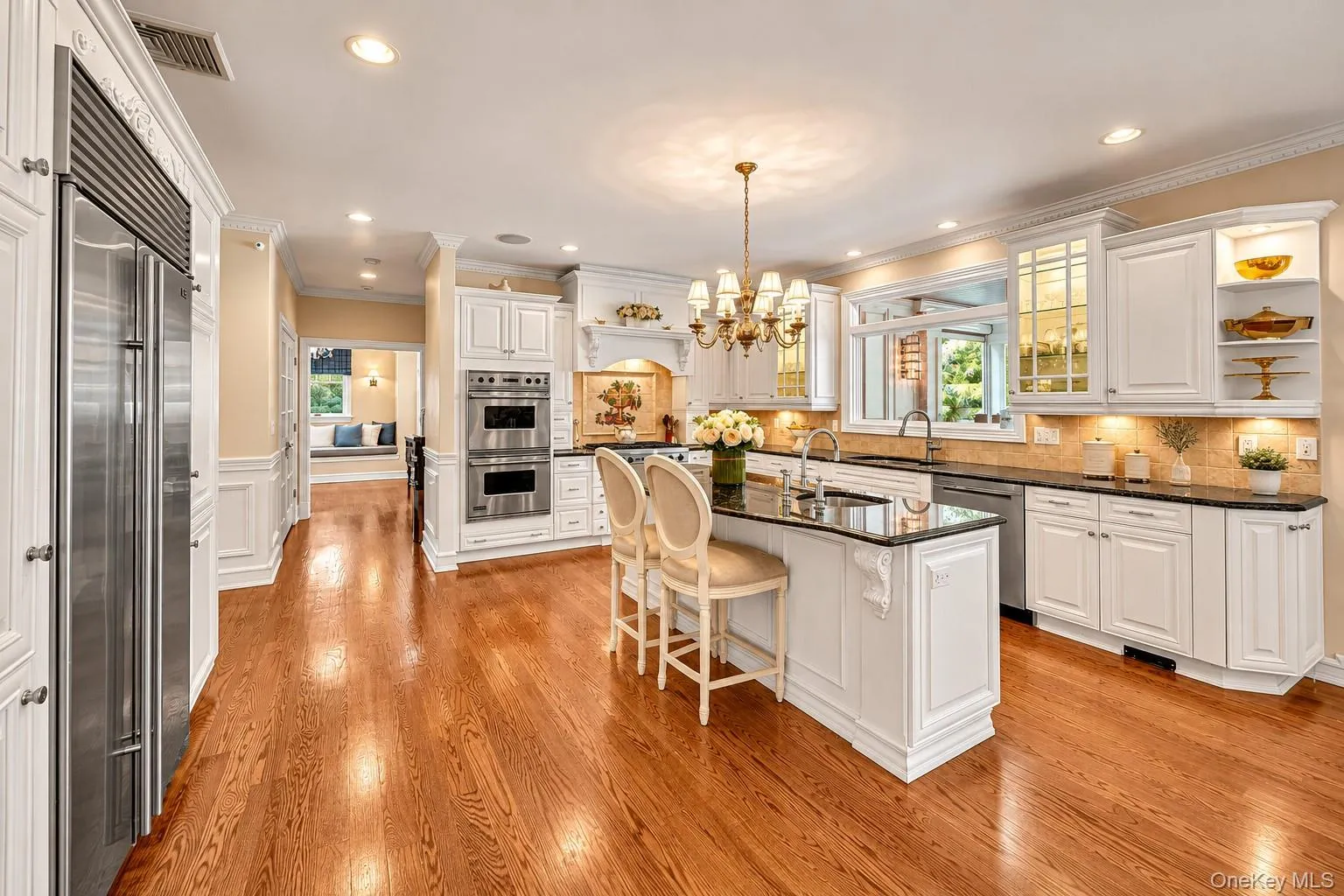 Hardwood flooring, stainless steel appliances, white cabinetry with crown molding, a kitchen island with seating, and recessed lighting Hardwood flooring, stainless steel appliances, white cabinetry with crown molding, a kitchen island with seating, and recessed lighting