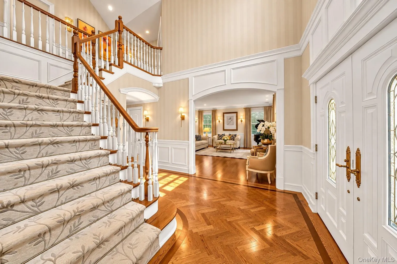 Grand foyer featuring a dual-level staircase with white balusters and wood handrails, herringbone wood flooring, decorative wall molding, and arched doorways Grand foyer featuring a dual-level staircase with white balusters and wood handrails, herringbone wood flooring, decorative wall molding, and arched doorways