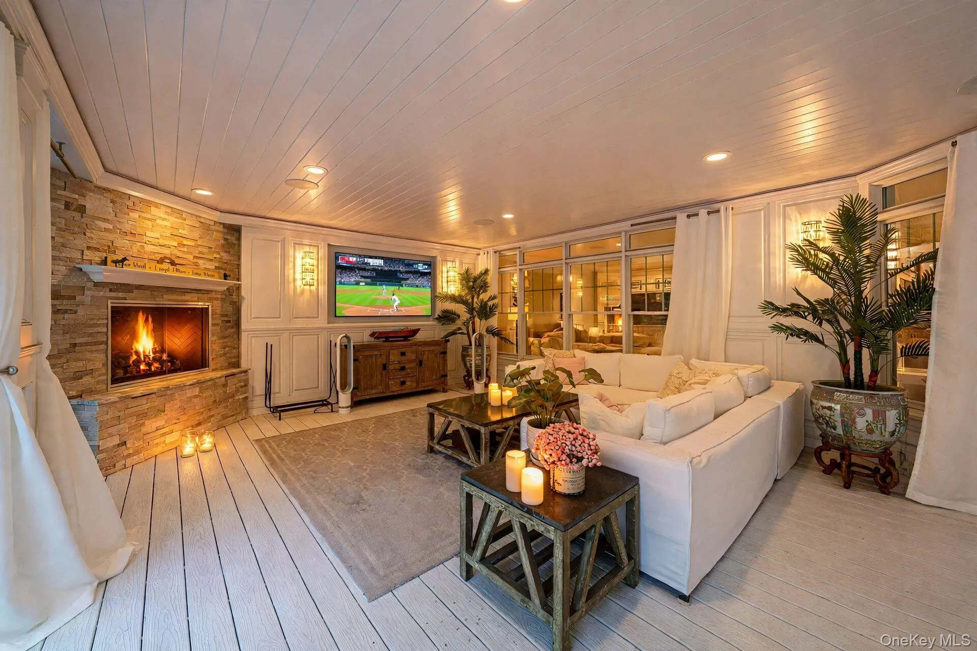 Spacious open-concept living area featuring a wood-burning fireplace with stone surround, wide-plank wood-finish flooring, coffered ceiling with recessed lighting, and a wall-mounted flat-screen television Spacious open-concept living area featuring a wood-burning fireplace with stone surround, wide-plank wood-finish flooring, coffered ceiling with recessed lighting, and a wall-mounted flat-screen television