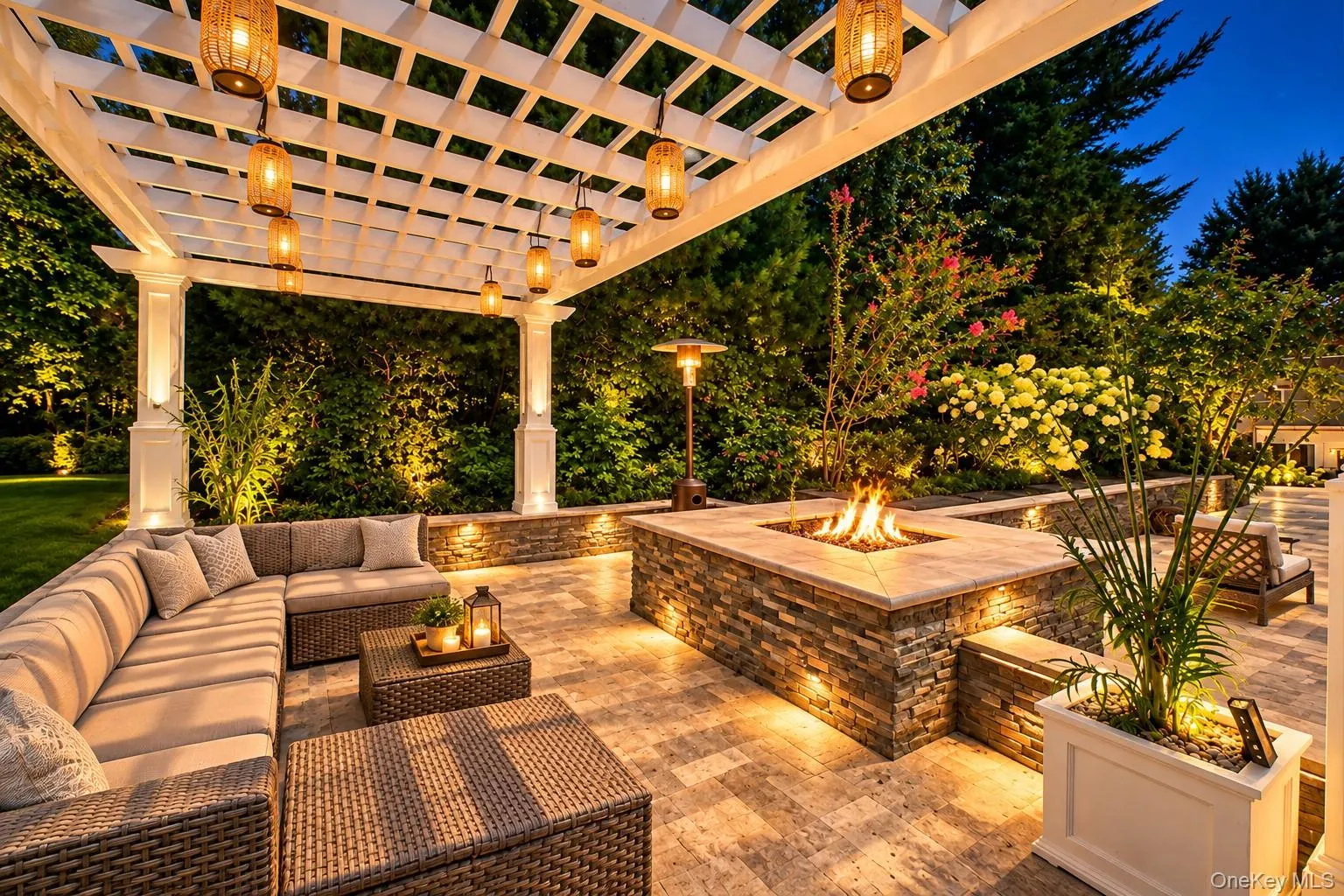 Expansive patio featuring a white pergola with hanging lanterns, a built-in stone fire pit, integrated lighting, and paver flooring Expansive patio featuring a white pergola with hanging lanterns, a built-in stone fire pit, integrated lighting, and paver flooring