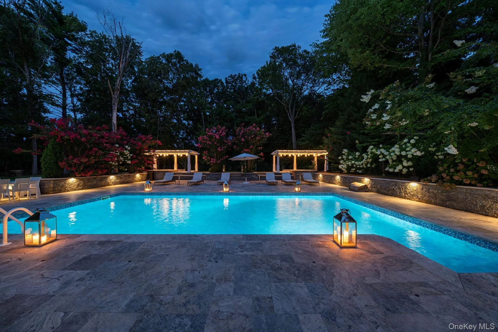 Inviting swimming pool with integrated lighting, extensive stone paver decking, retaining walls, and pergola structures Inviting swimming pool with integrated lighting, extensive stone paver decking, retaining walls, and pergola structures
