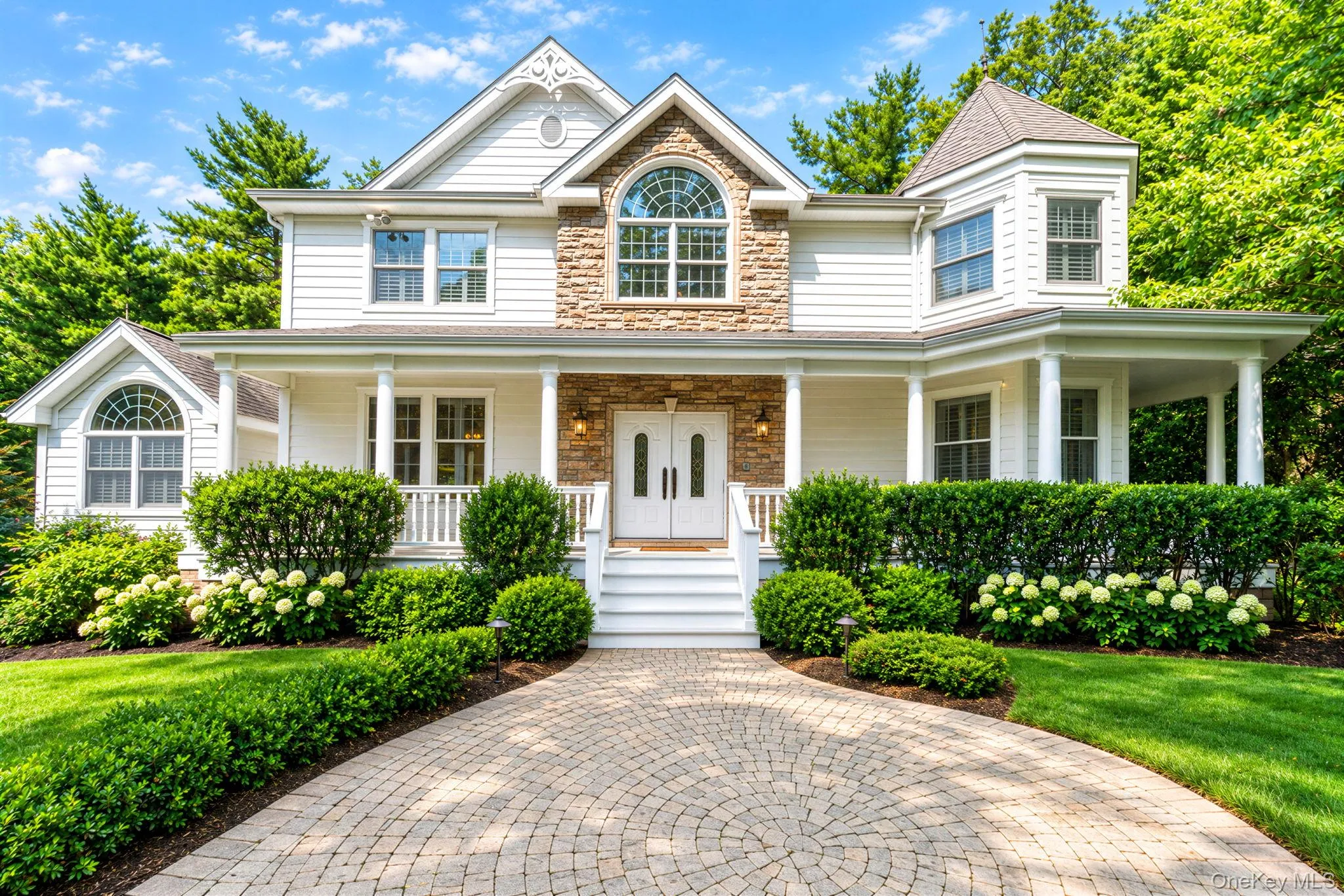 Classic Colonial-style residence featuring a brick and stone facade with white siding, arched entryway with decorative transom window, and a covered front porch Classic Colonial-style residence featuring a brick and stone facade with white siding, arched entryway with decorative transom window, and a covered front porch