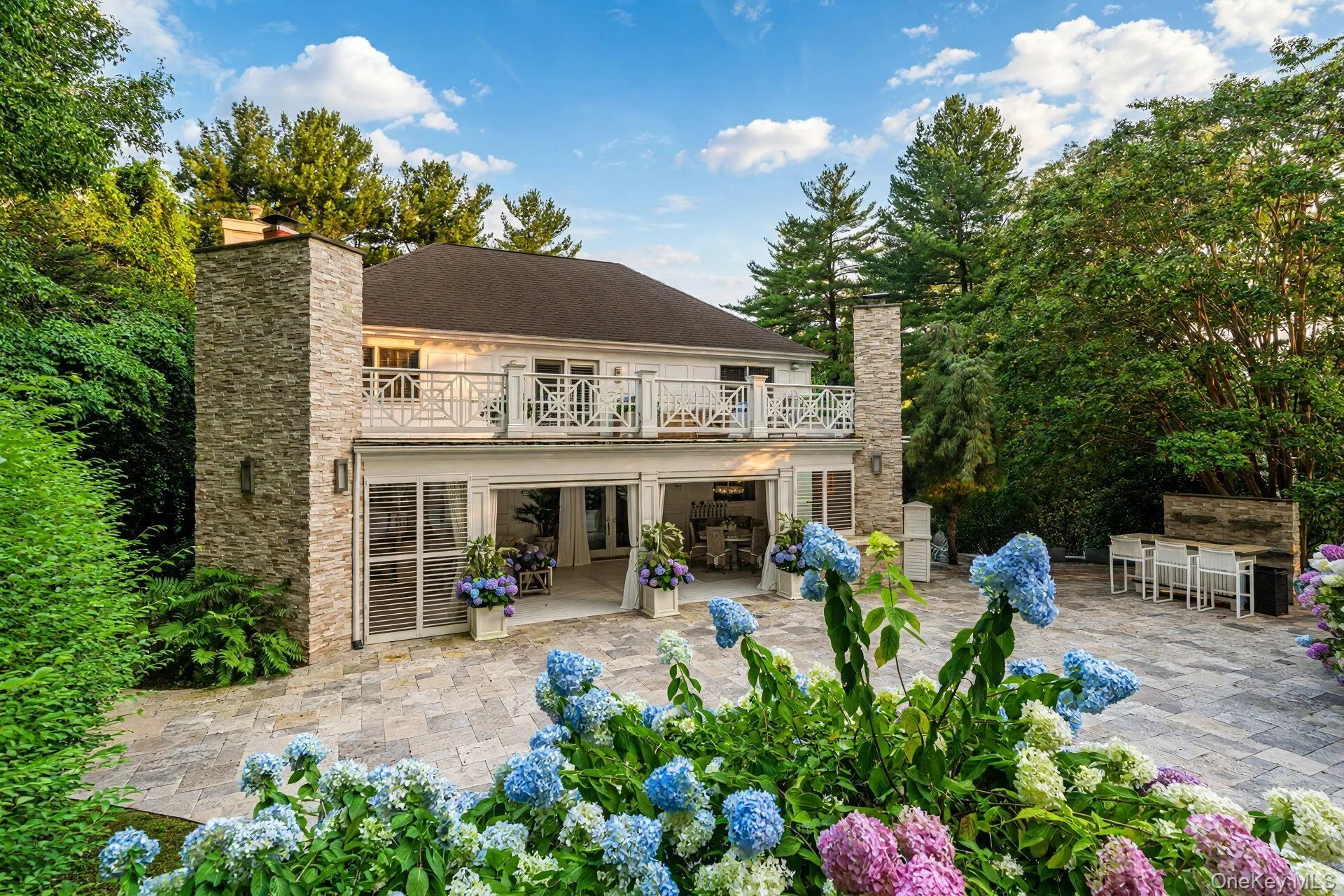 Elegant brick Colonial with a sophisticated rear elevation featuring a two-story stone facade, decorative balustrade, and expansive patio in stone-finish hardscape Elegant brick Colonial with a sophisticated rear elevation featuring a two-story stone facade, decorative balustrade, and expansive patio in stone-finish hardscape