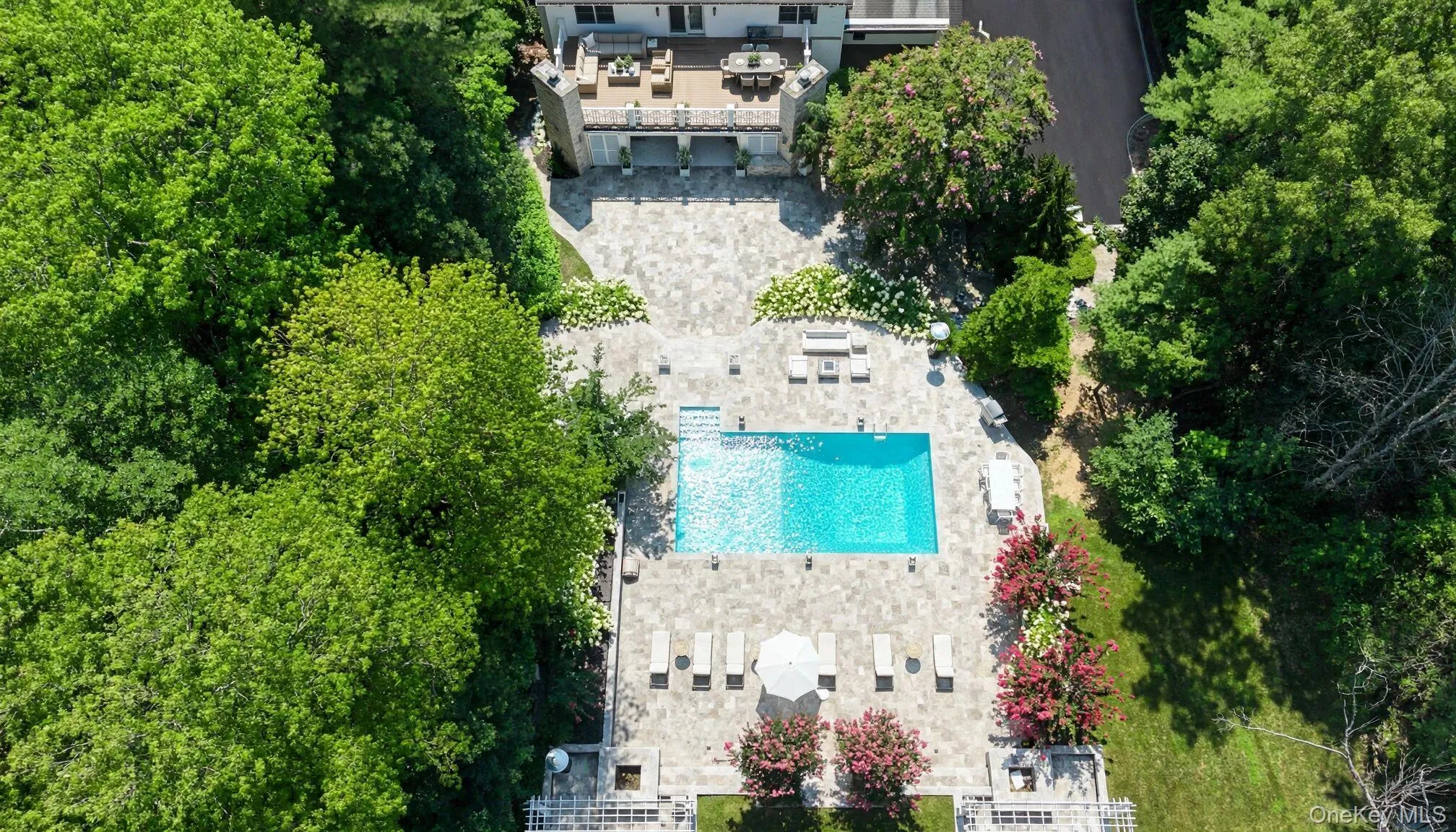 Expansive outdoor living space featuring a rectangular swimming pool, extensive paver patio, and mature landscaping Expansive outdoor living space featuring a rectangular swimming pool, extensive paver patio, and mature landscaping