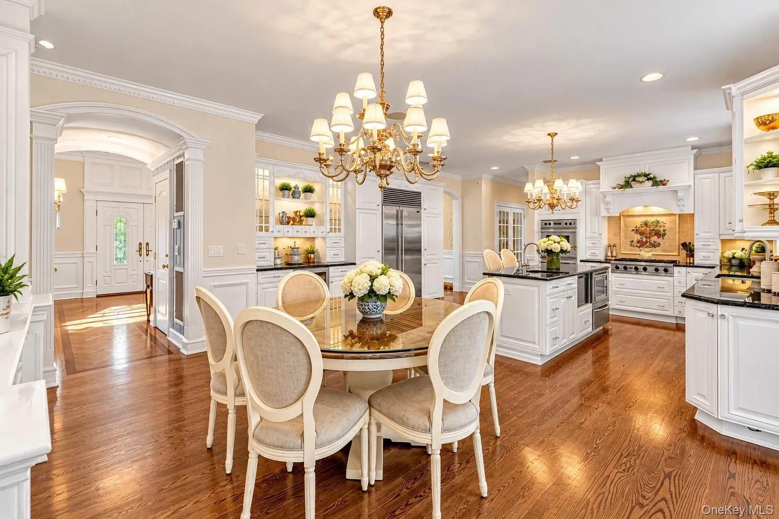 Spacious open-concept kitchen with wood-finish flooring, white cabinetry, dark countertops, and a central island with a sink Spacious open-concept kitchen with wood-finish flooring, white cabinetry, dark countertops, and a central island with a sink