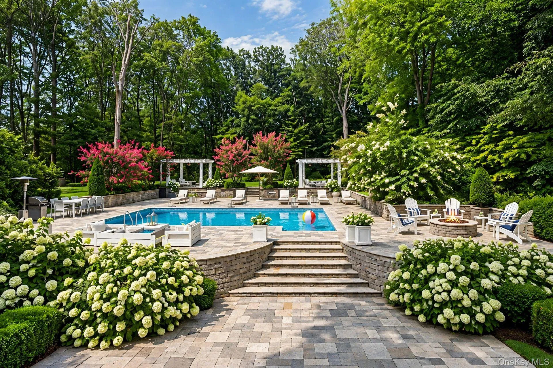 Expansive outdoor living area featuring a swimming pool, stone paver patio, integrated fire pit, and tiered landscaping Expansive outdoor living area featuring a swimming pool, stone paver patio, integrated fire pit, and tiered landscaping