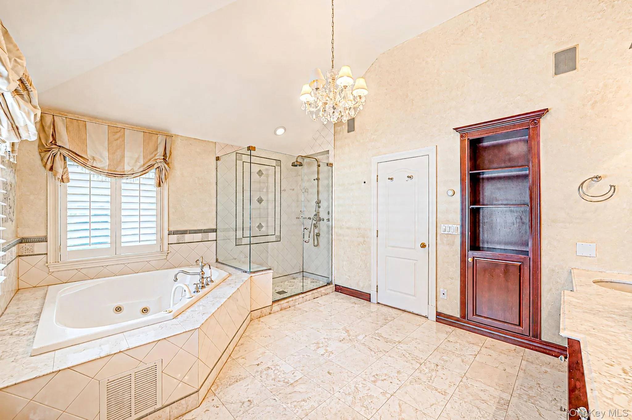 Jetted soaking tub with tile surround, glass-enclosed shower, built-in shelving, and chandelier lighting Jetted soaking tub with tile surround, glass-enclosed shower, built-in shelving, and chandelier lighting