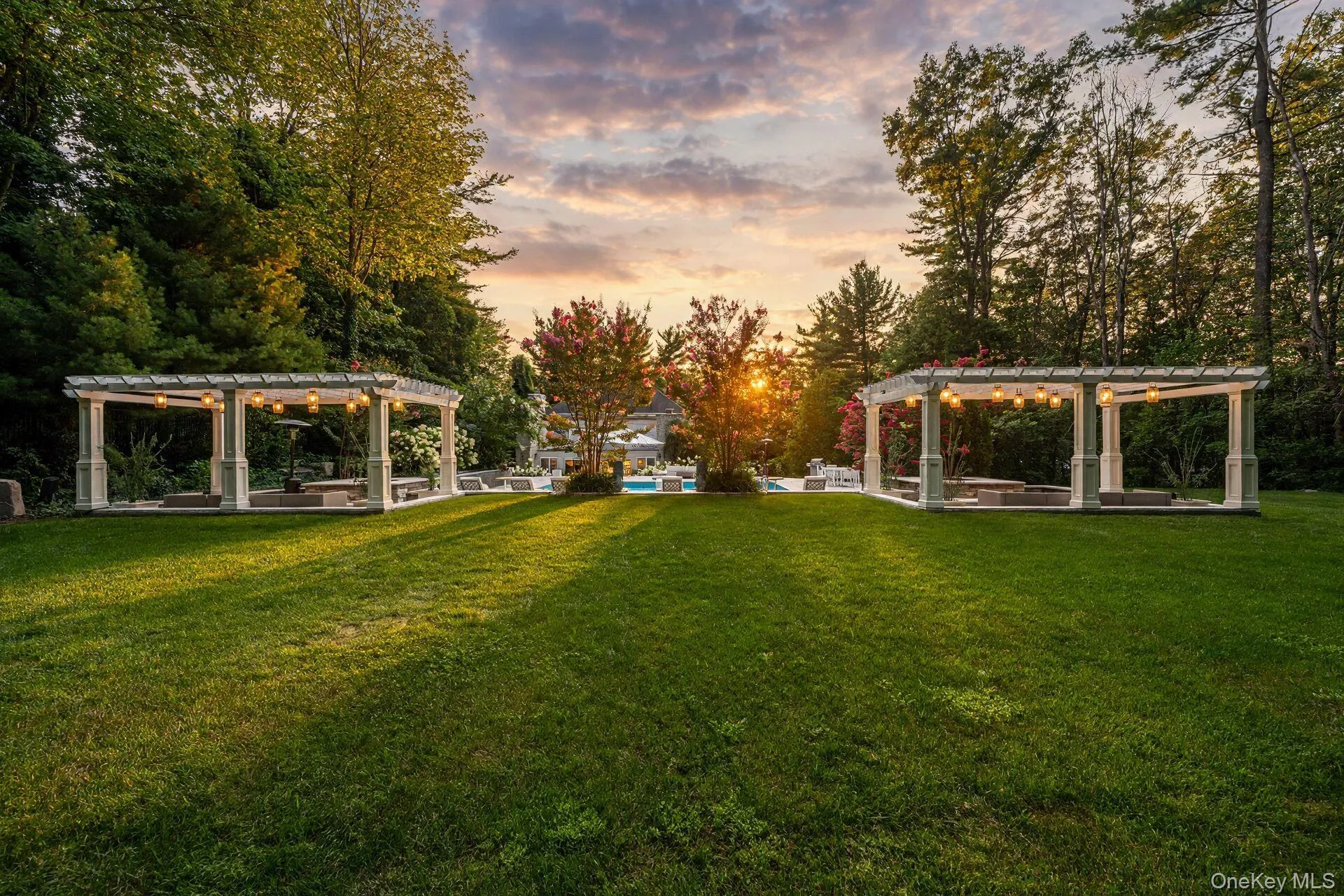 Expansive lawn featuring two white pergolas with integrated lighting, bordered by mature trees and verdant landscaping Expansive lawn featuring two white pergolas with integrated lighting, bordered by mature trees and verdant landscaping
