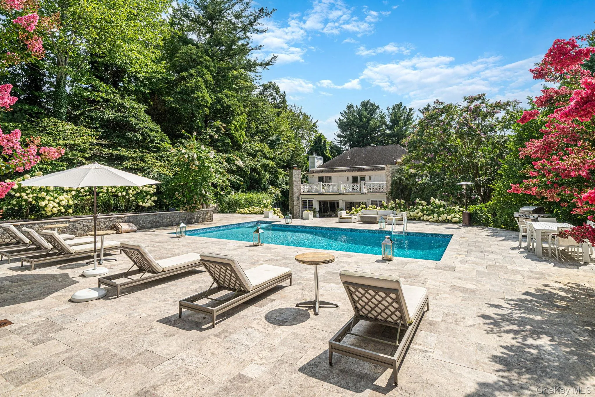 Expansive hardscape patio featuring a resort-style saltwater swimming pool with integrated spa, multiple lounge chairs, and market umbrellas Expansive hardscape patio featuring a resort-style saltwater swimming pool with integrated spa, multiple lounge chairs, and market umbrellas