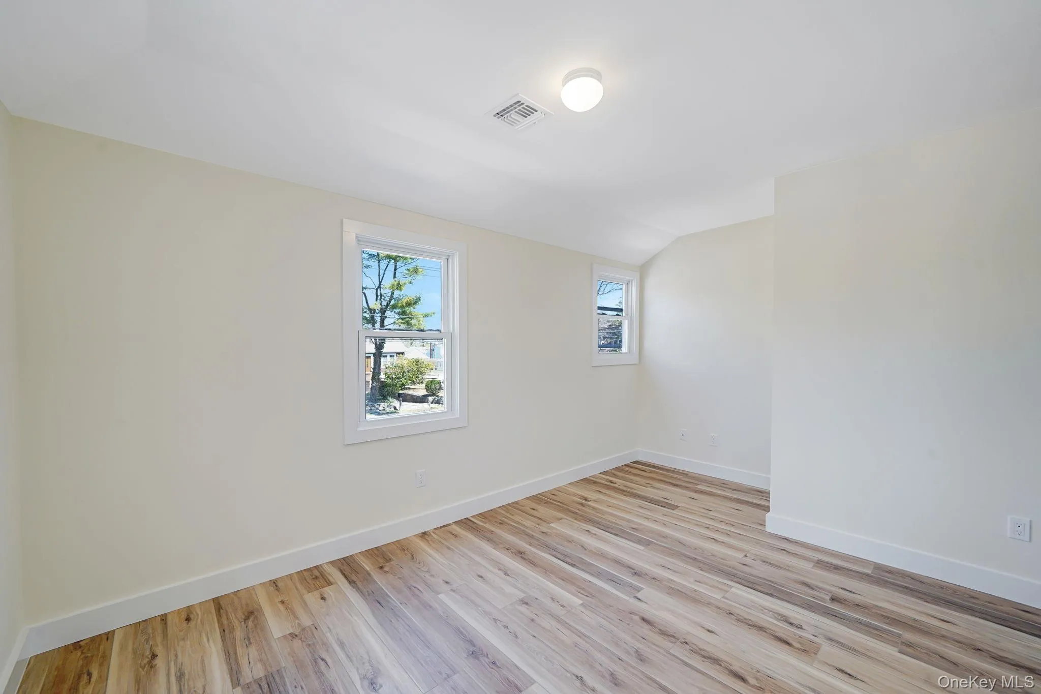 Unfurnished room featuring baseboards, light wood-style floors, and lofted ceiling Unfurnished room featuring baseboards, light wood-style floors, and lofted ceiling